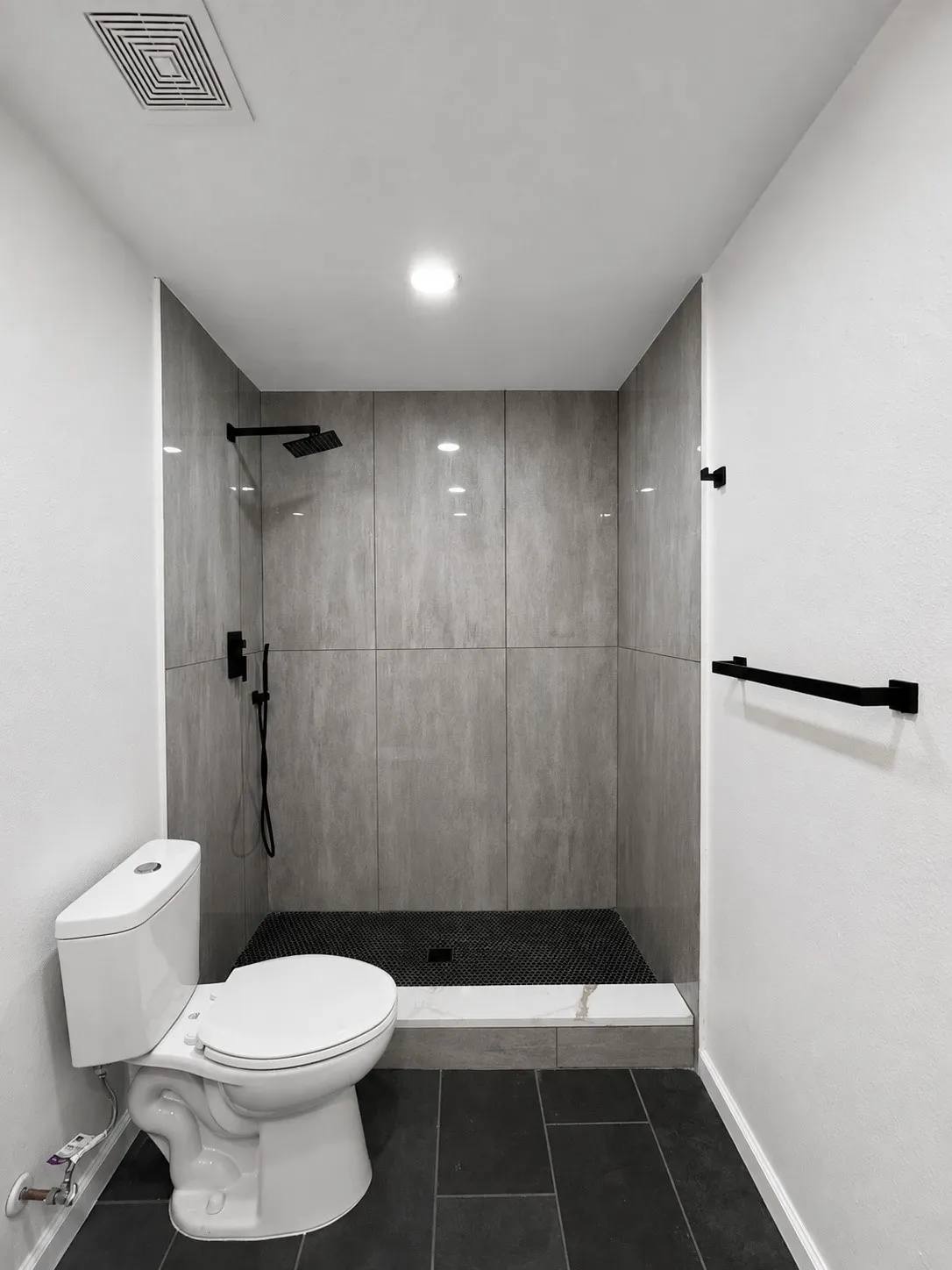 Contemporary walk-in shower with vertical gray wall tiling, black penny tile shower floor, and matte black fixtures