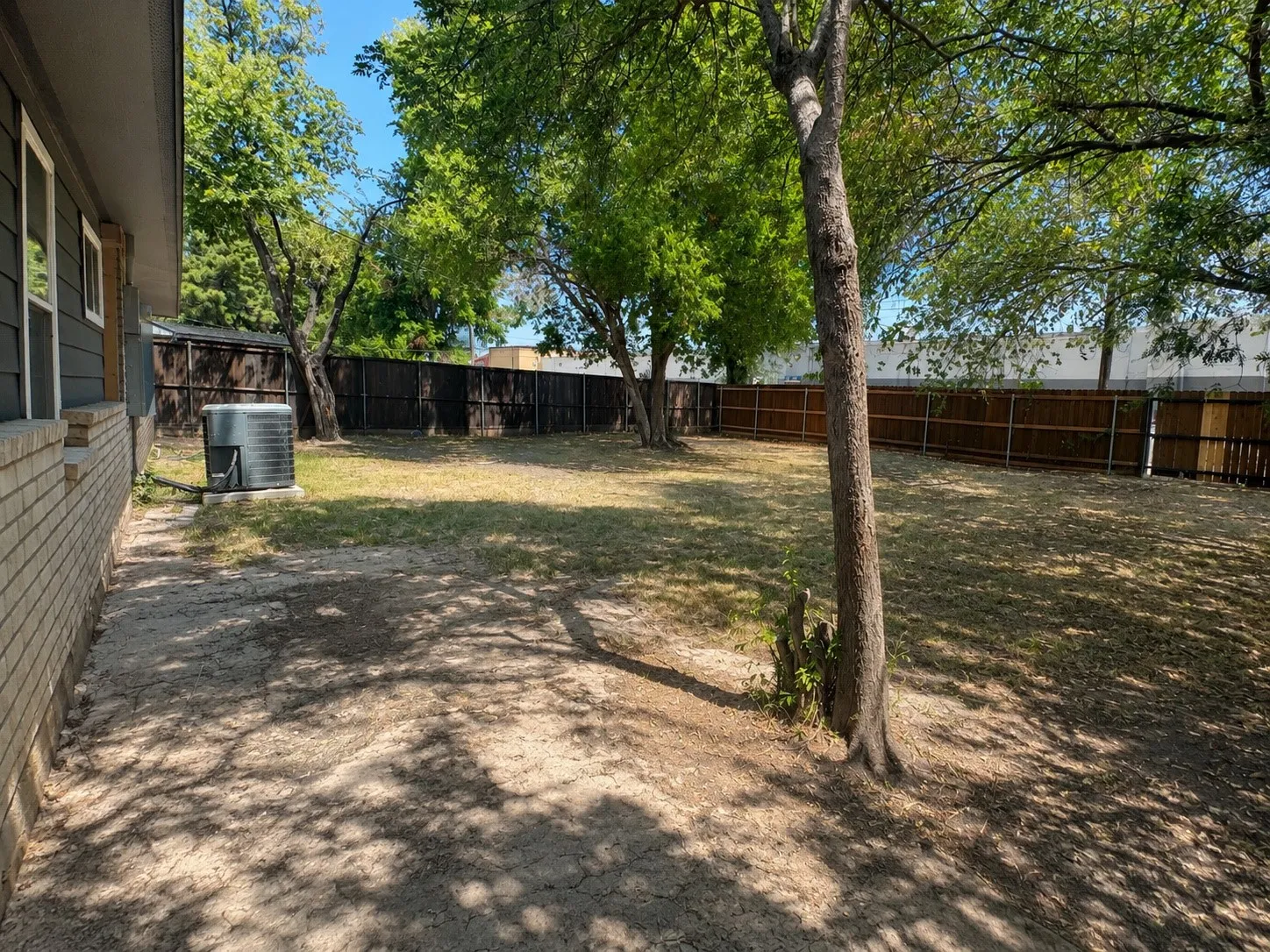 Expansive backyard with a full privacy fence, mature trees, and a brick and siding exterior