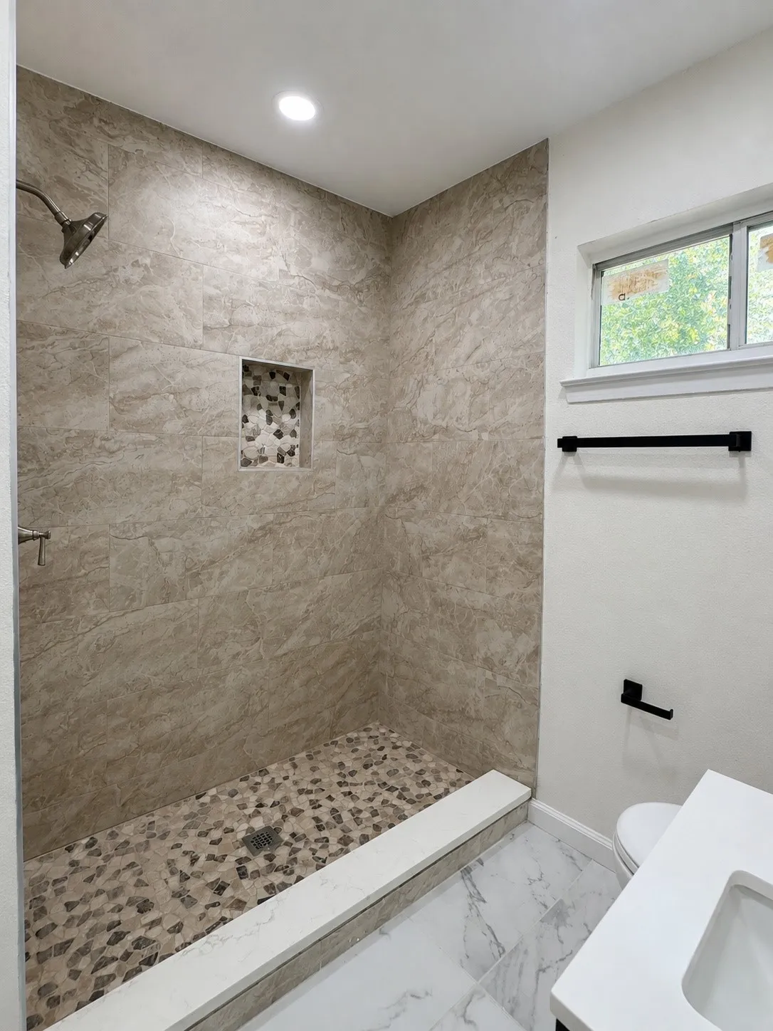 Walk-in shower with natural stone-look wall tile and a pebble floor