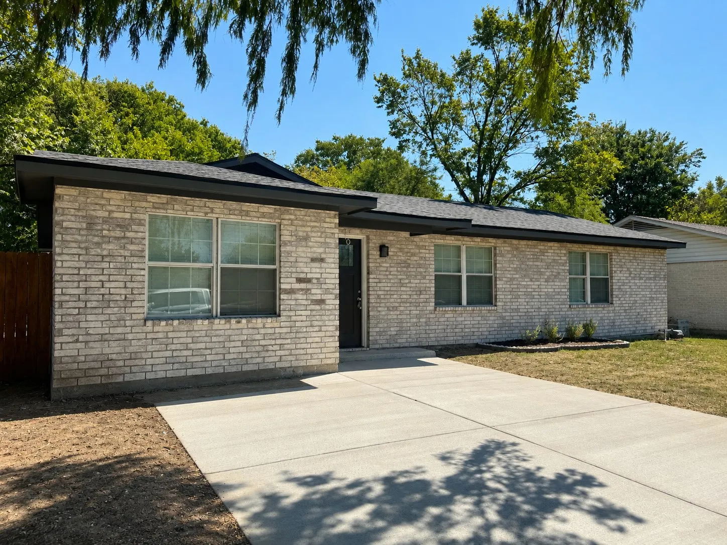 Light brick facade with dark trim, asphalt shingle roof, and a concrete driveway