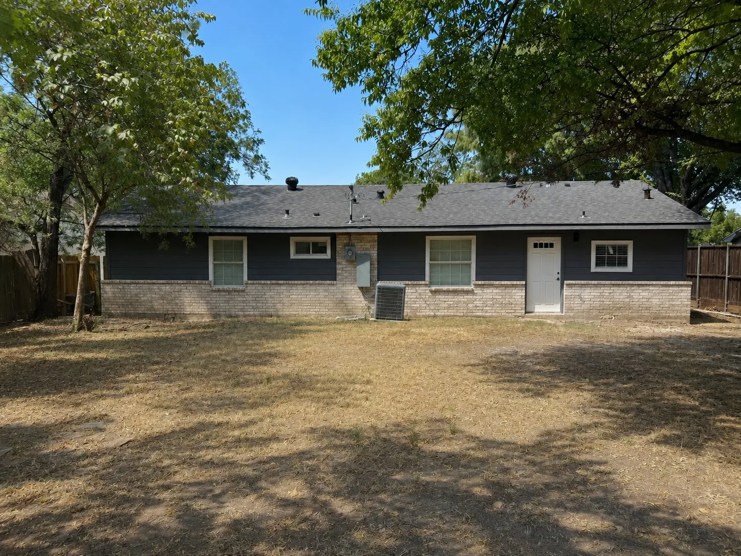 Rear exterior featuring dark gray siding, light-toned brick wainscoting, and white trim windows