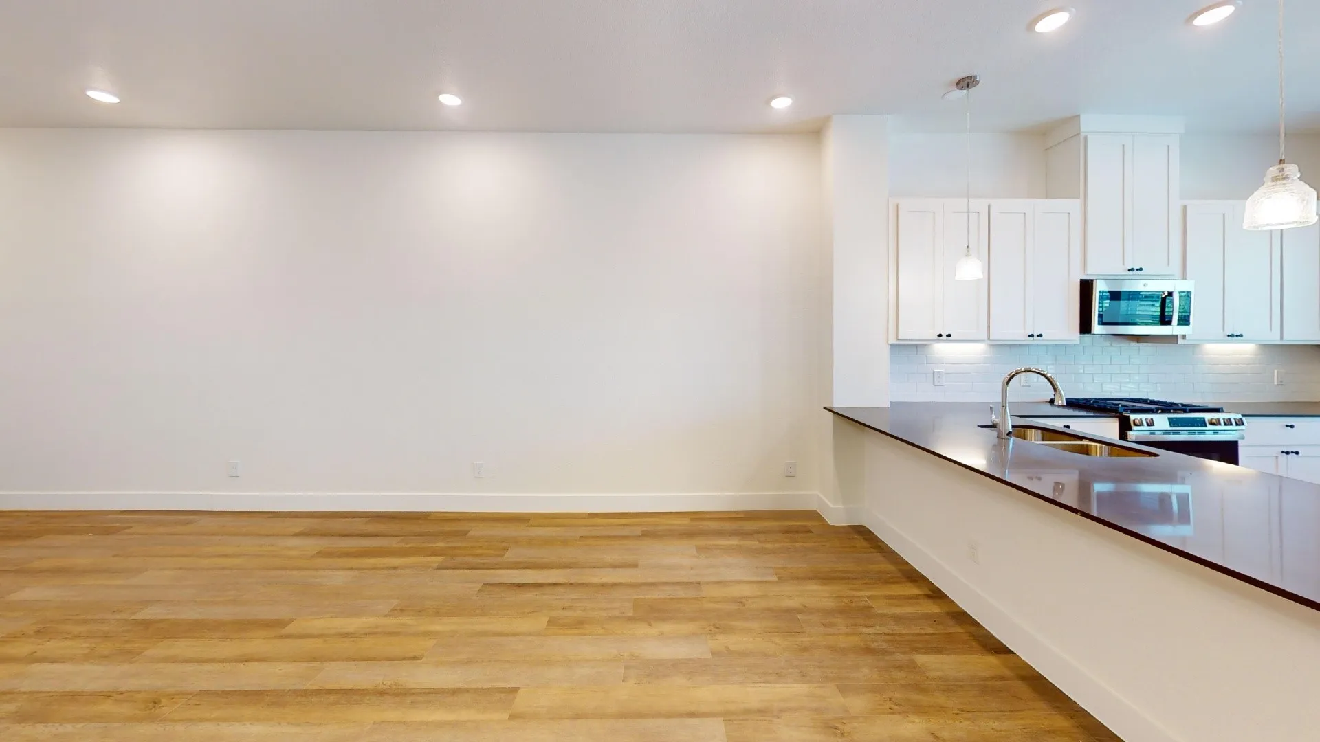 Wood-finish flooring, recessed ceiling lighting, kitchen island with sink, stainless steel appliances, and white cabinetry