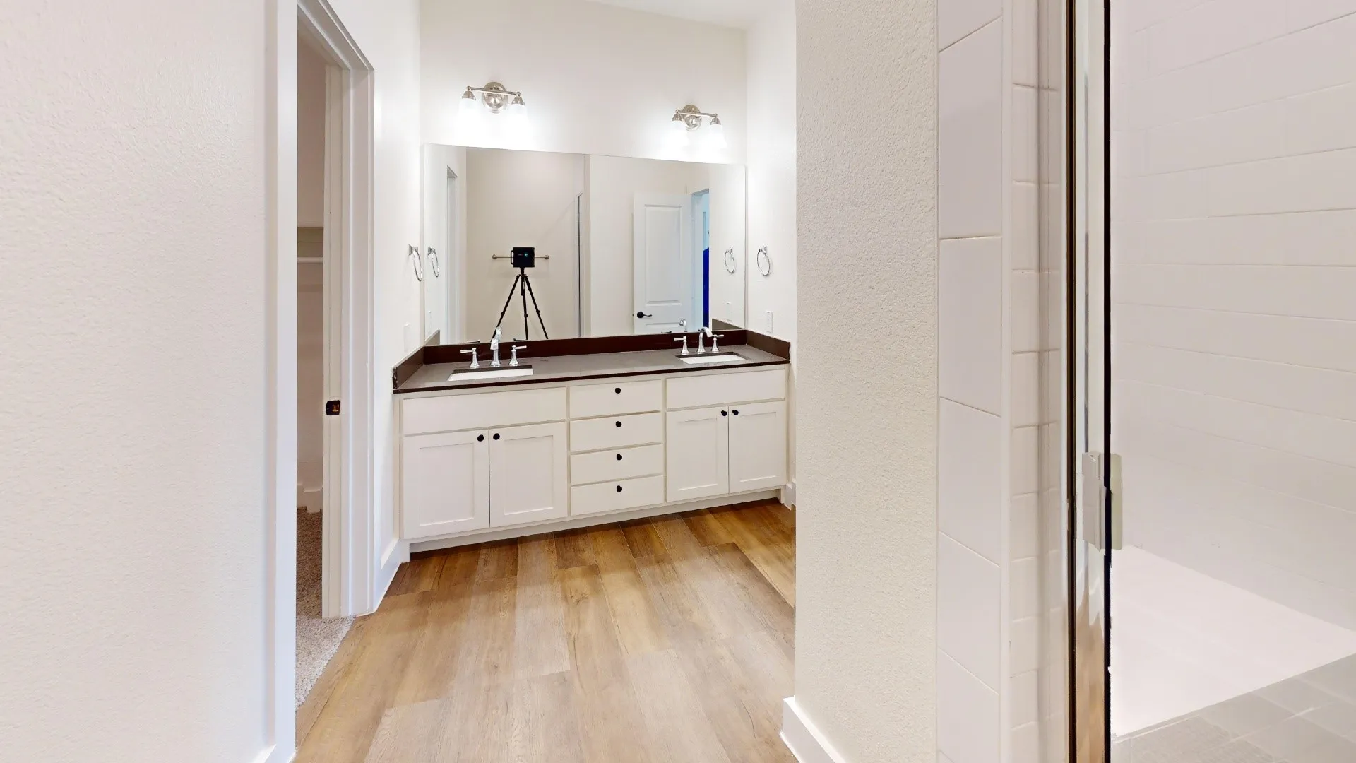 Wood-finish flooring with a dual vanity featuring white cabinetry and dark countertops