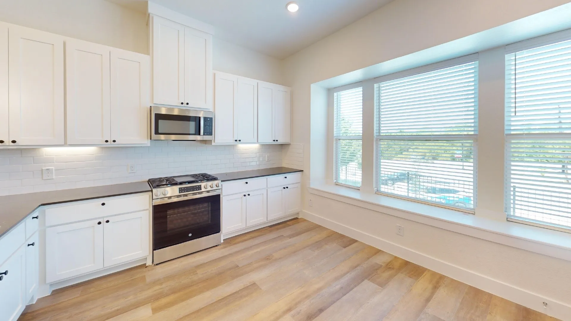 Kitchen featuring white shaker cabinetry, stainless steel appliances, light gray countertops, white subway tile backsplash, and wood-finish flooring