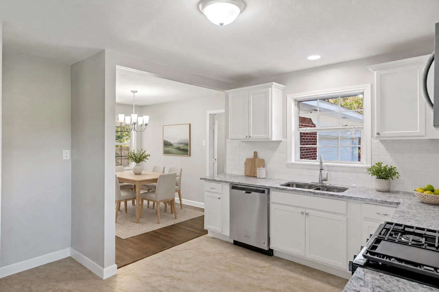 Kitchen featuring white shaker cabinetry, stainless steel dishwasher, undermount sink with a gooseneck faucet, light-toned countertops, and a white subway tile backsplash