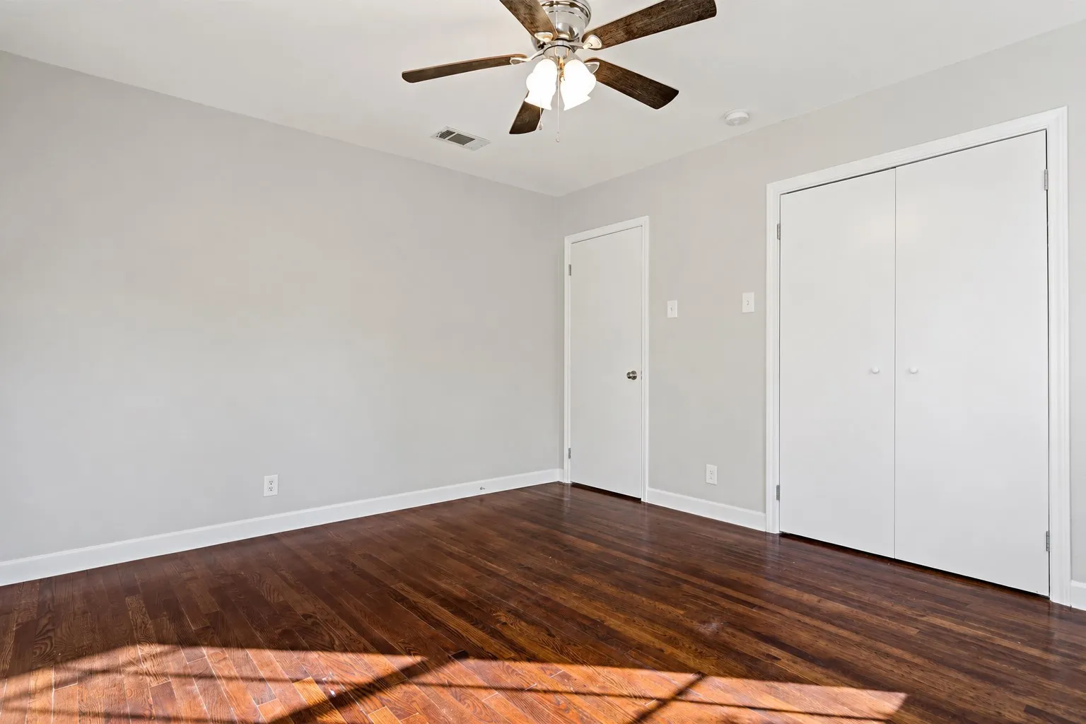 Wood-finish flooring, white walls, ceiling fan with light fixture, and double-door closet