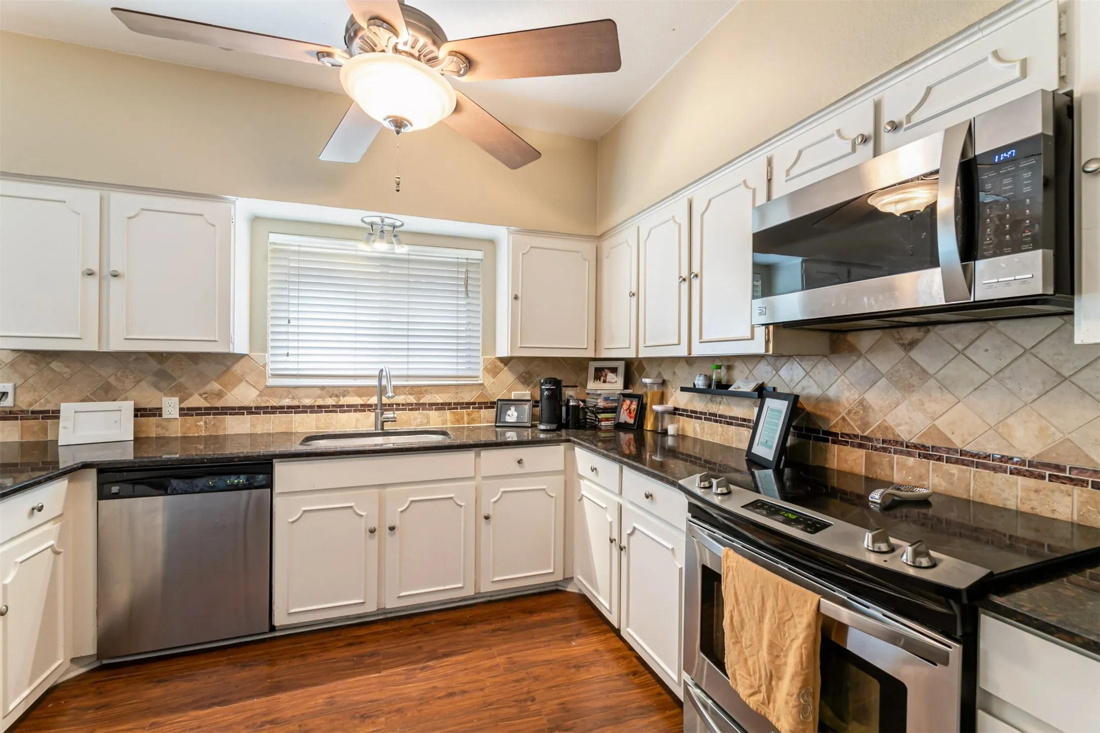 Kitchen featuring white cabinetry, black countertops, stainless steel appliances, and a tiled backsplash