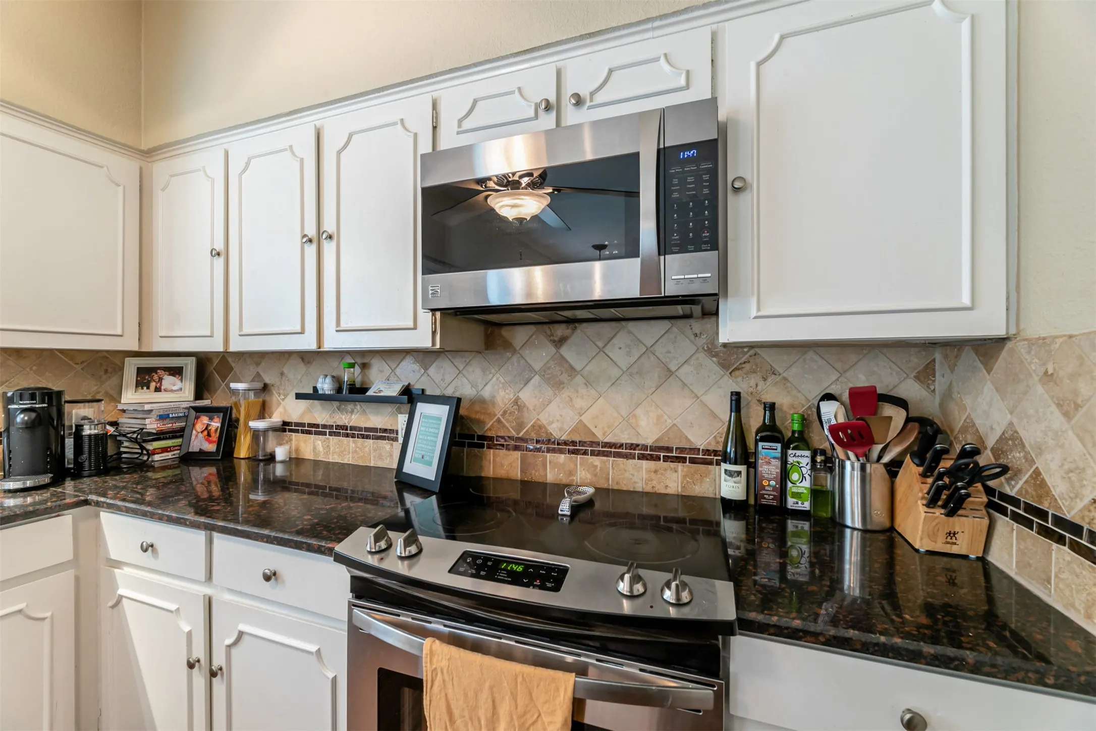 White cabinetry with traditional detailing, dark countertop, stainless steel appliances, and a tiled backsplash