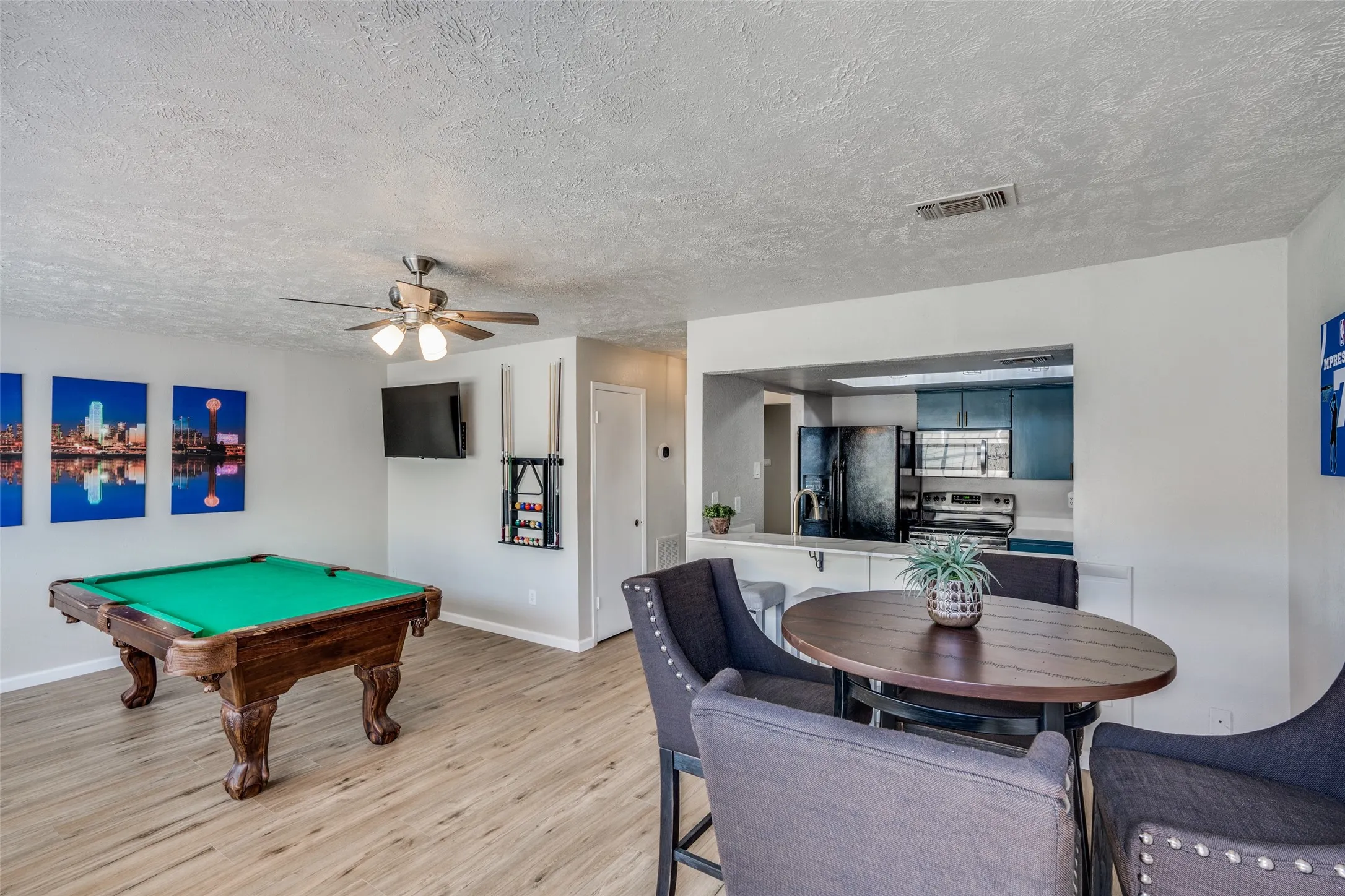 Open-concept living area with wood-finish flooring, a ceiling fan, and a kitchen pass-through with a breakfast bar