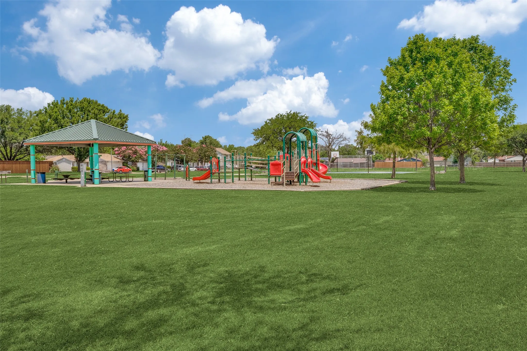 Expansive grassy area with a covered pavilion, multi-structure playground, and mature trees