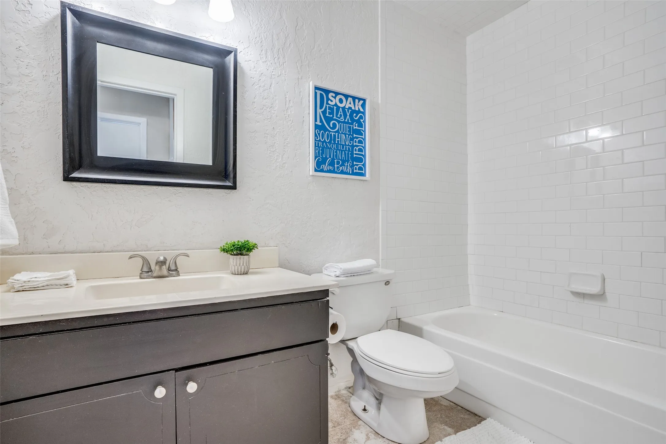 White subway tile tub surround, built-in bathtub, vanity with a rectangular sink, dual-handle faucet, and framed mirror