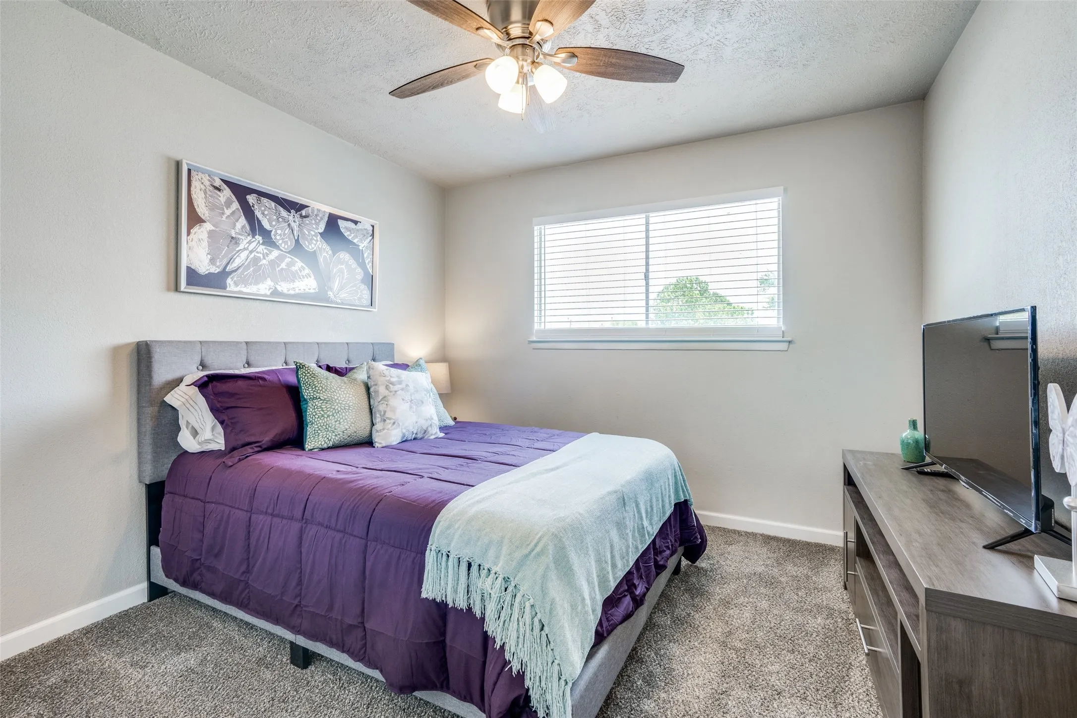 Textured walls, carpeted flooring, window with blinds, and a ceiling fan with integrated lighting