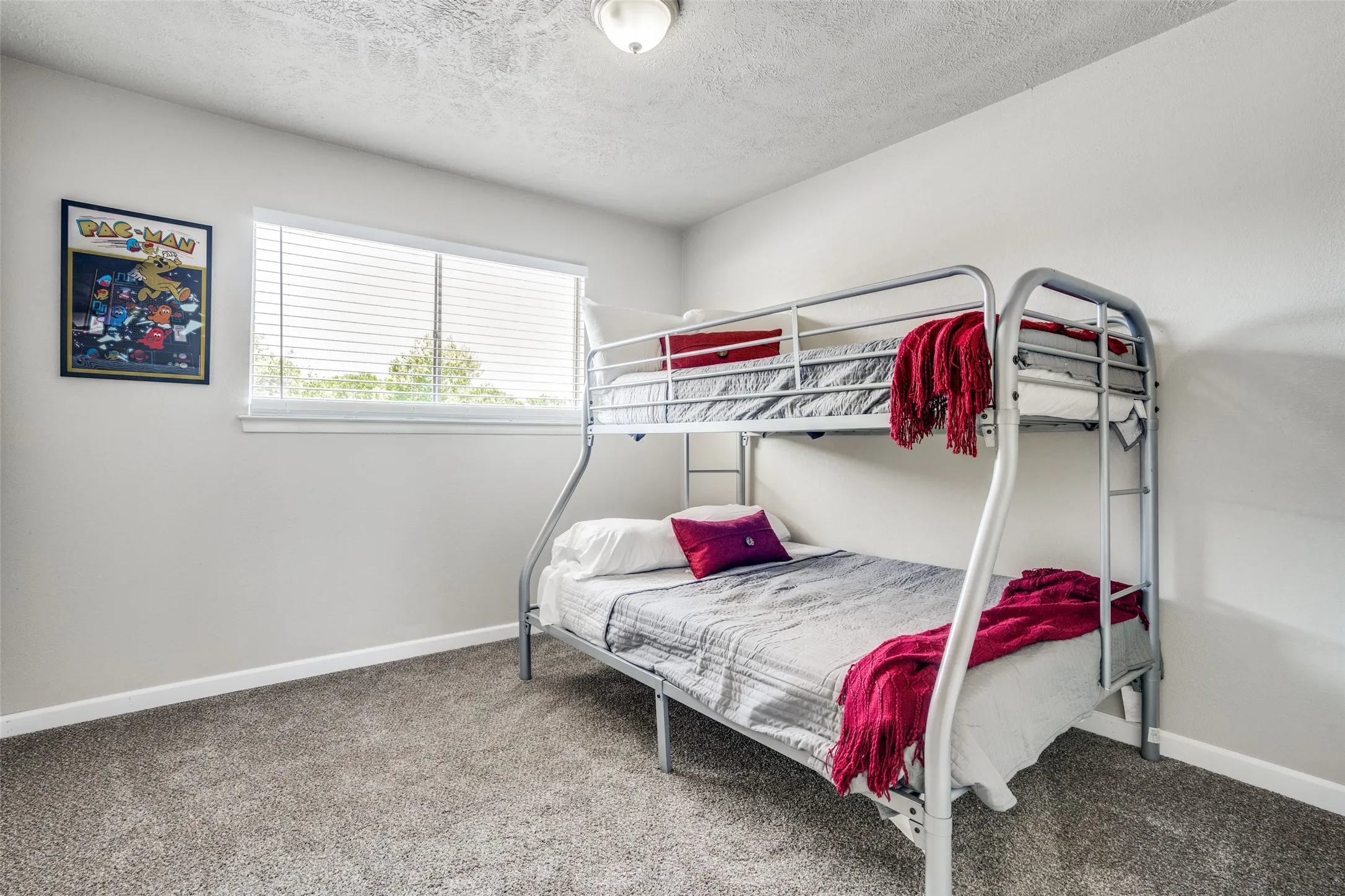 White walls, gray carpet flooring, and a single window with white blinds