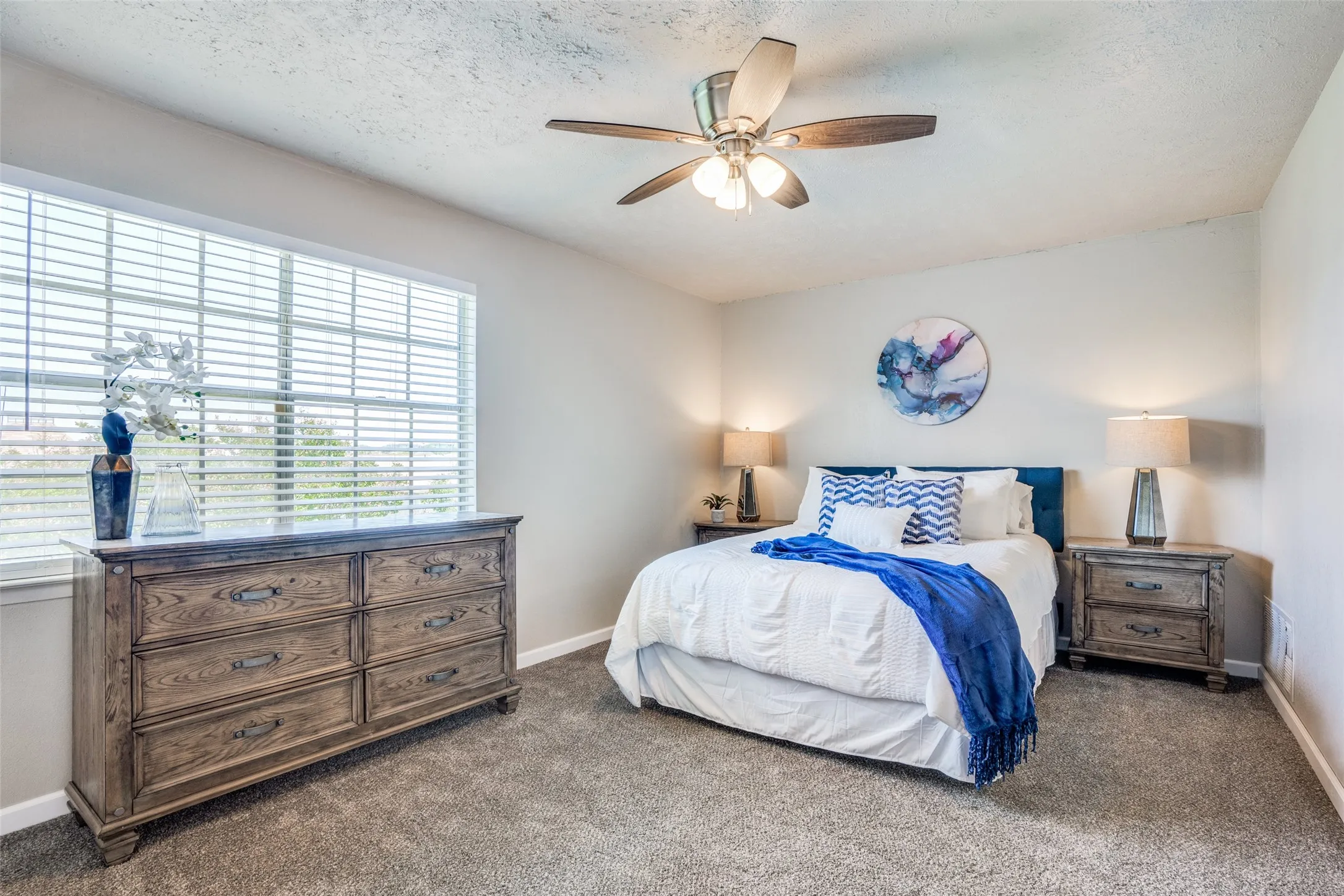 Spacious room featuring broad window with blinds, ceiling fan, and carpet flooring