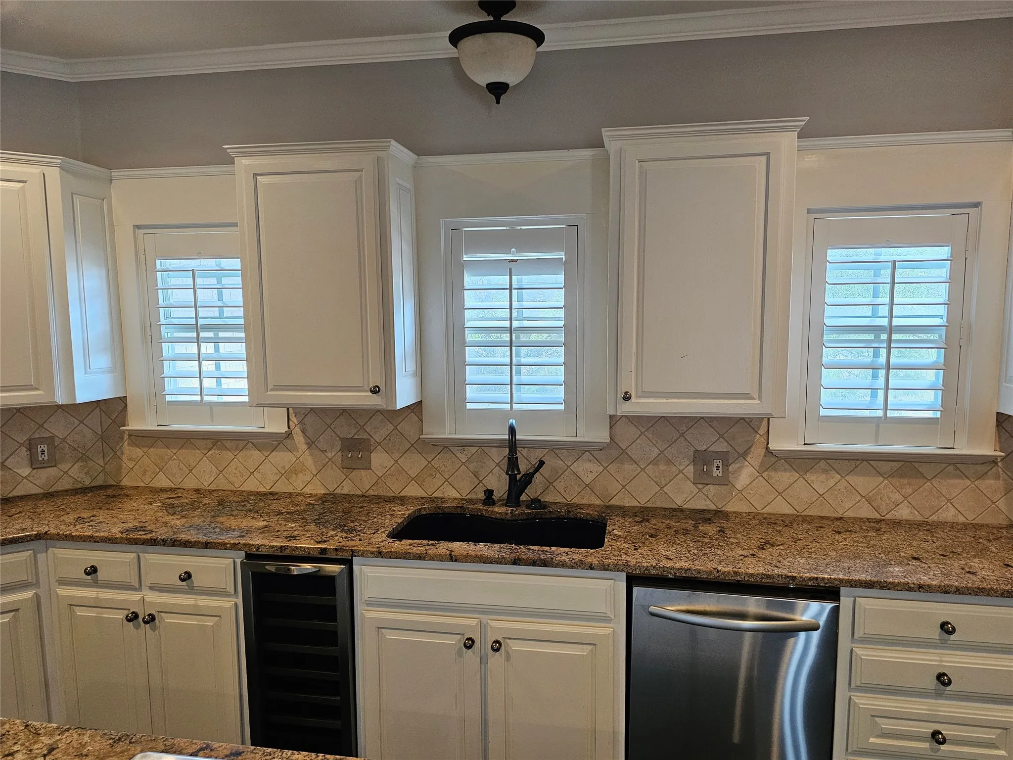 White cabinetry, granite countertops, decorative tile backsplash, stainless steel dishwasher, and a built-in beverage refrigerator