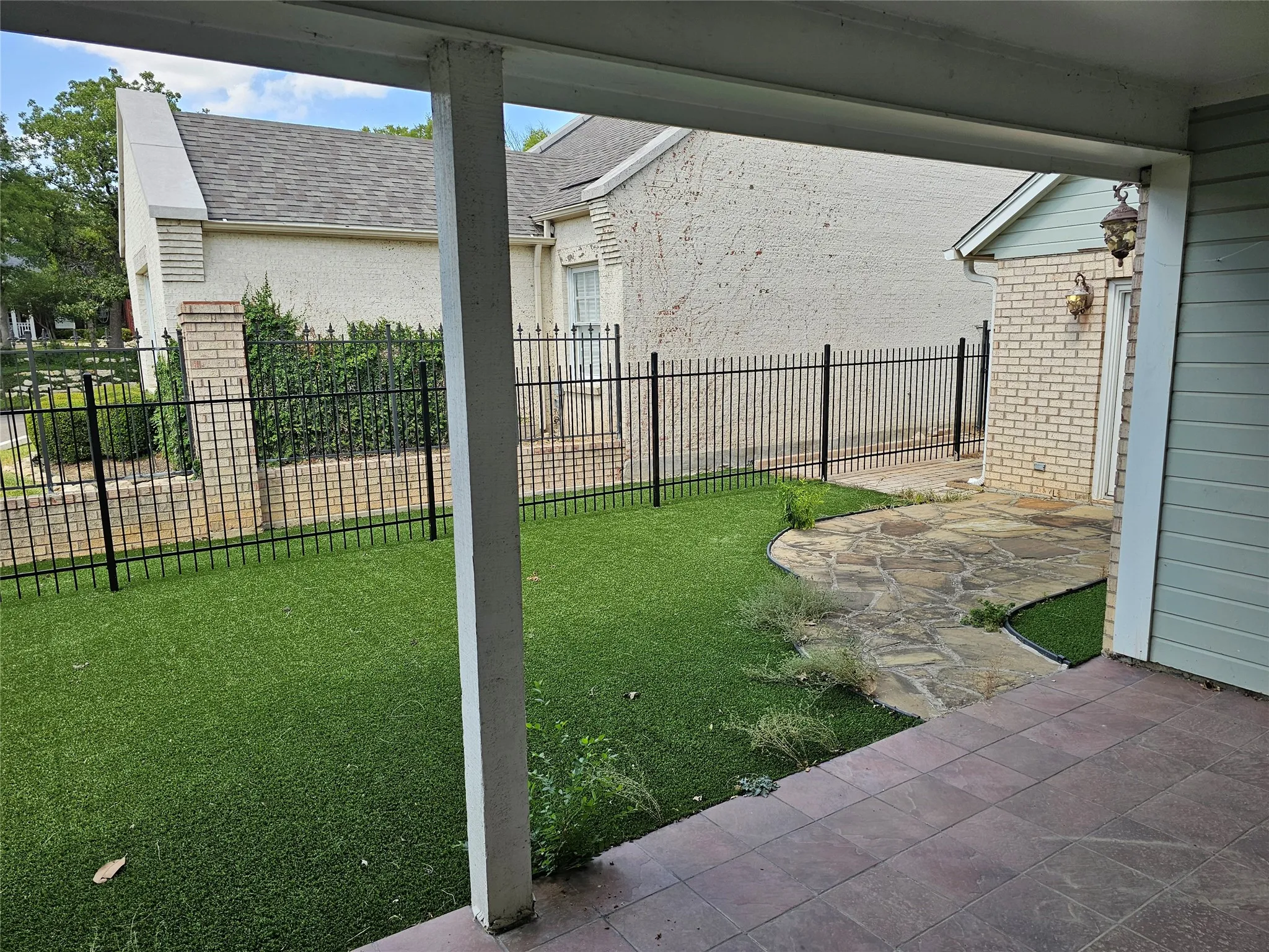 Paved patio, artificial turf, flagstone pathway, black metal fencing, and brick wall accents