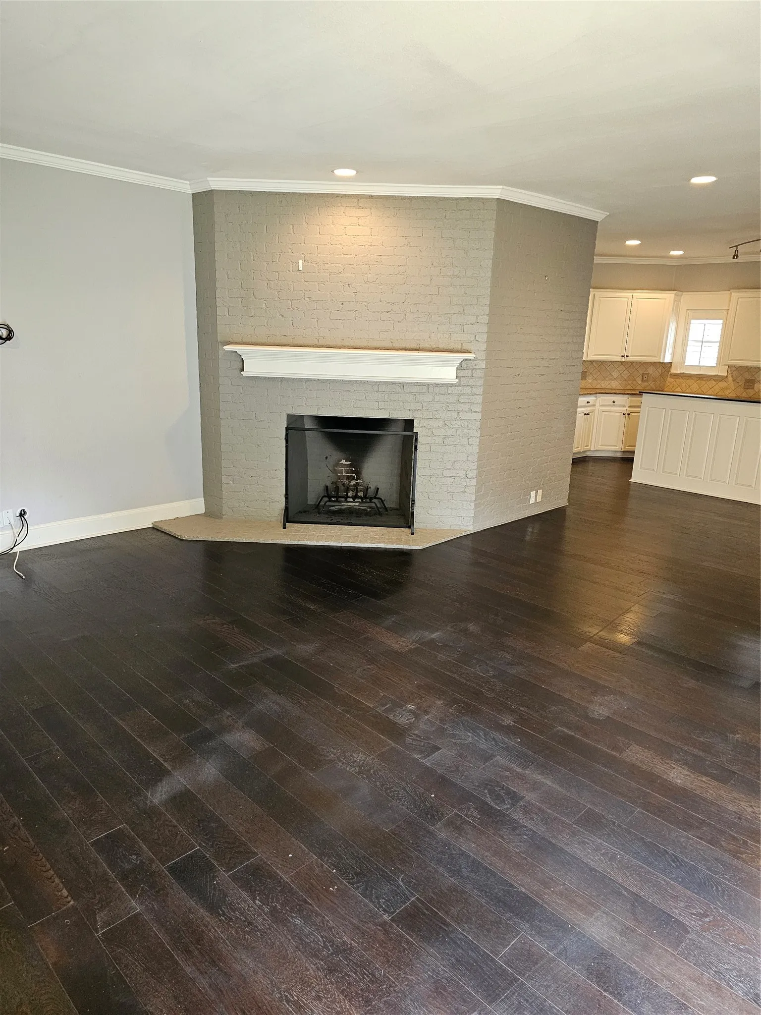 Brick fireplace with mantel and hearth, dark wood-finish flooring, recessed lighting, and crown molding