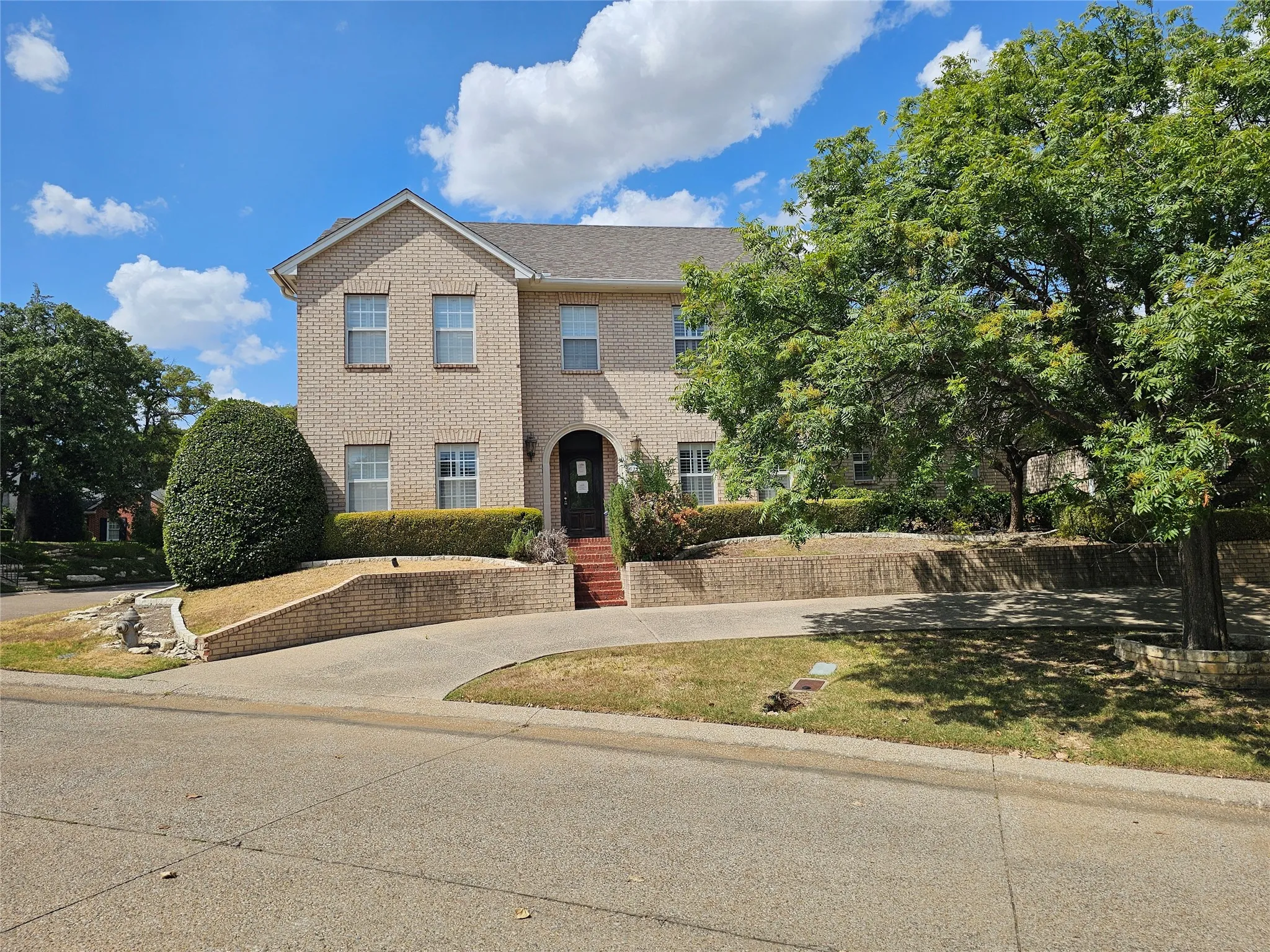 Two-story brick exterior with an arched entryway, mature tree, and concrete driveway