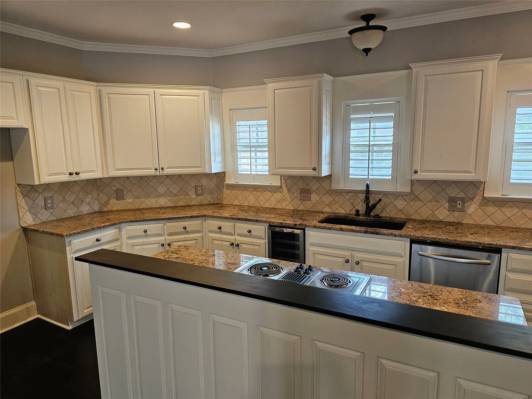 White cabinetry with dark hardware, stone countertops, tiled backsplash, stainless steel dishwasher, and built-in cooktop