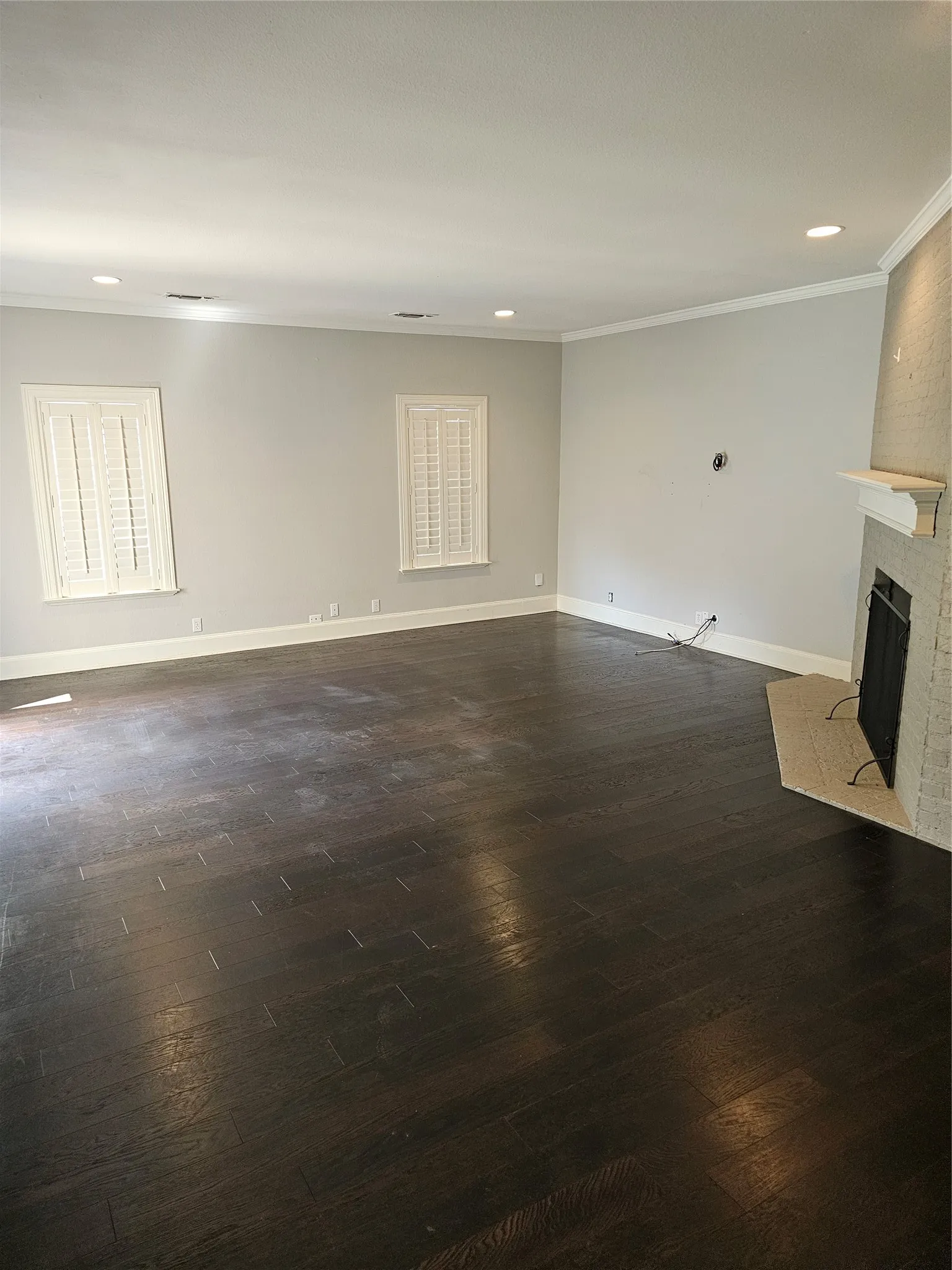Recessed lighting, crown molding, plantation shutters, wood-finish flooring, and a brick fireplace with a mantle