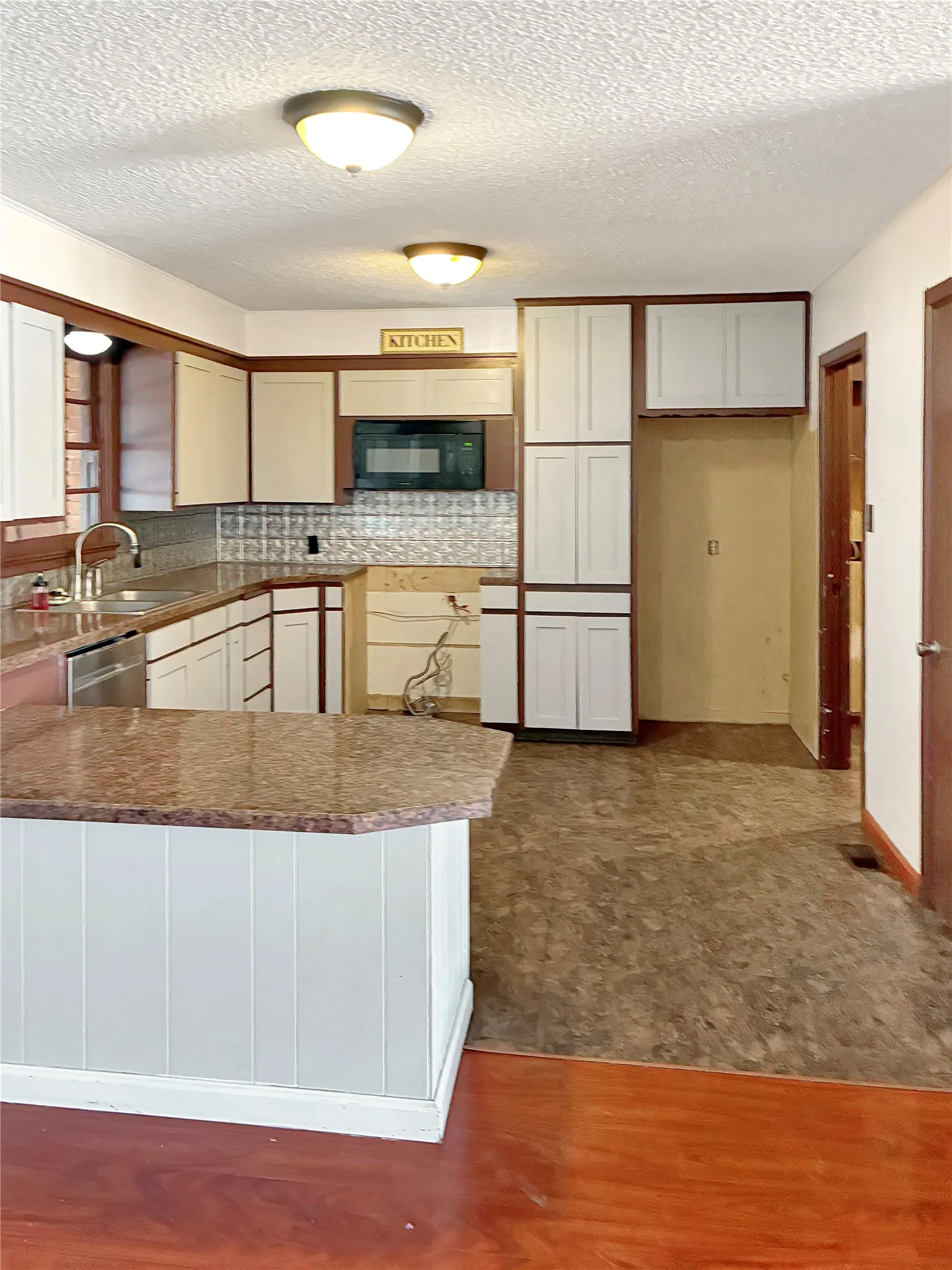 Kitchen featuring white cabinetry, dark wood-finish trim, a built-in microwave, and a breakfast bar with a stone-finish countertop