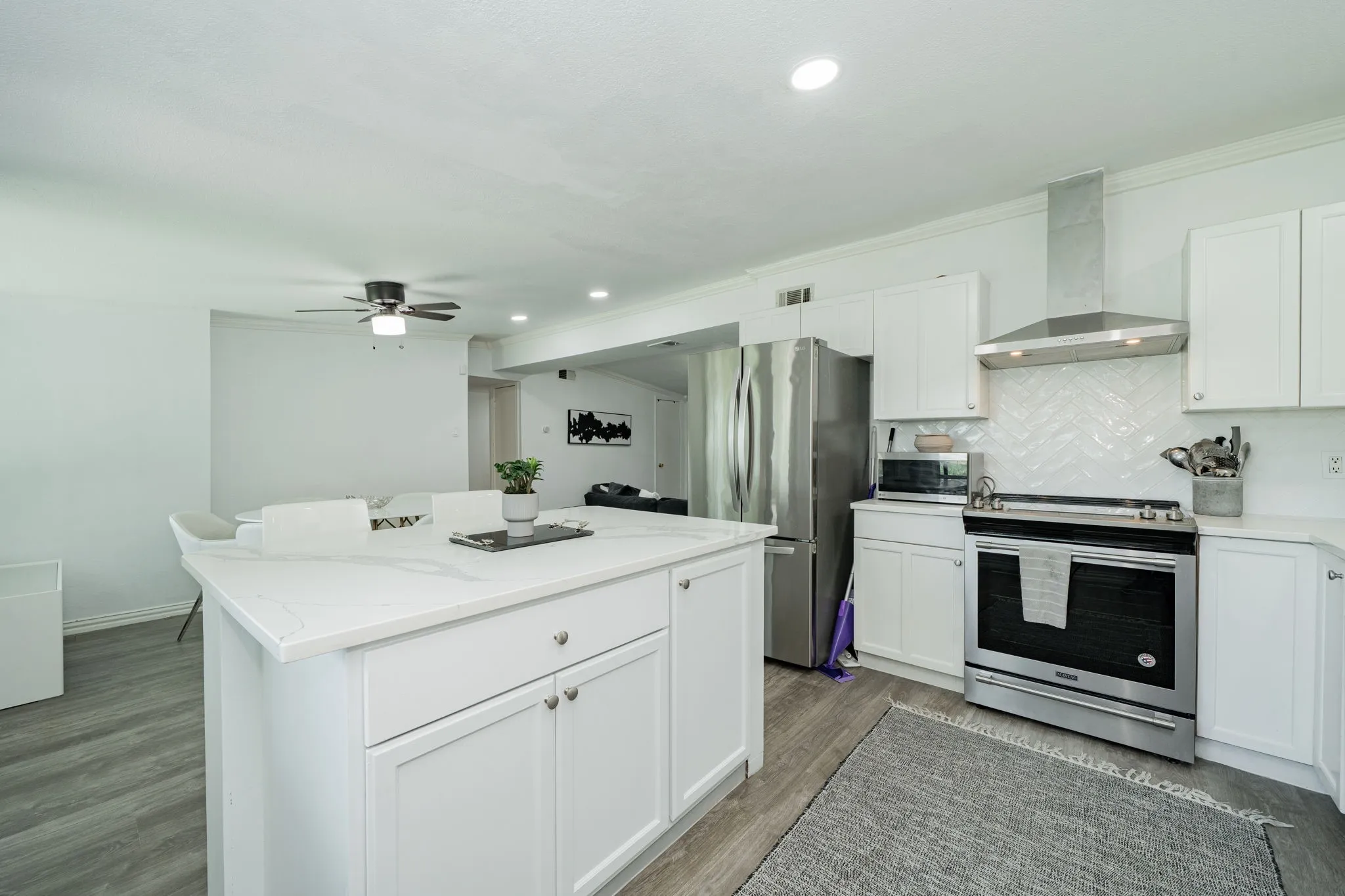 Kitchen featuring stainless steel appliances, wall chimney exhaust hood, backsplash, white cabinetry, and crown molding