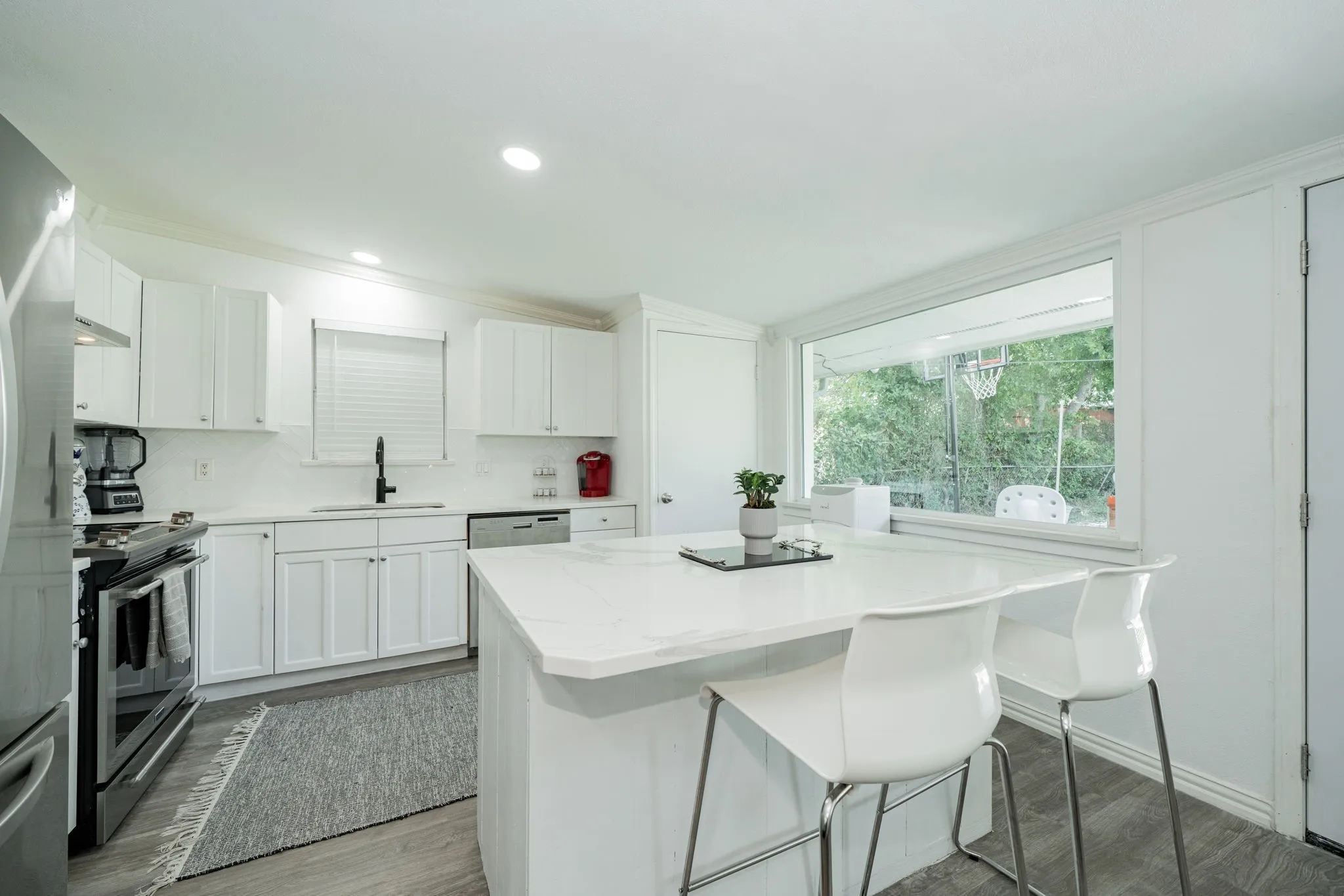 Kitchen featuring appliances with stainless steel finishes, wood finished floors, white cabinetry, a center island, and recessed lighting