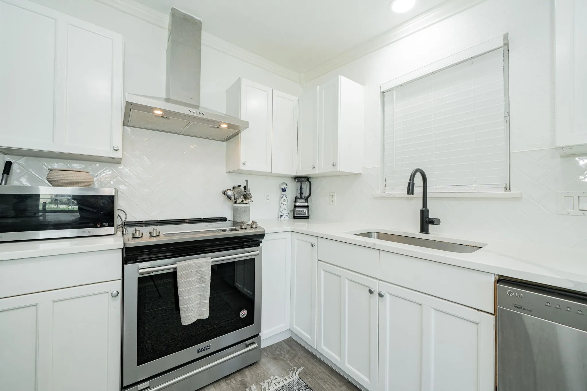 Kitchen with appliances with stainless steel finishes, wall chimney exhaust hood, crown molding, tasteful backsplash, and white cabinetry