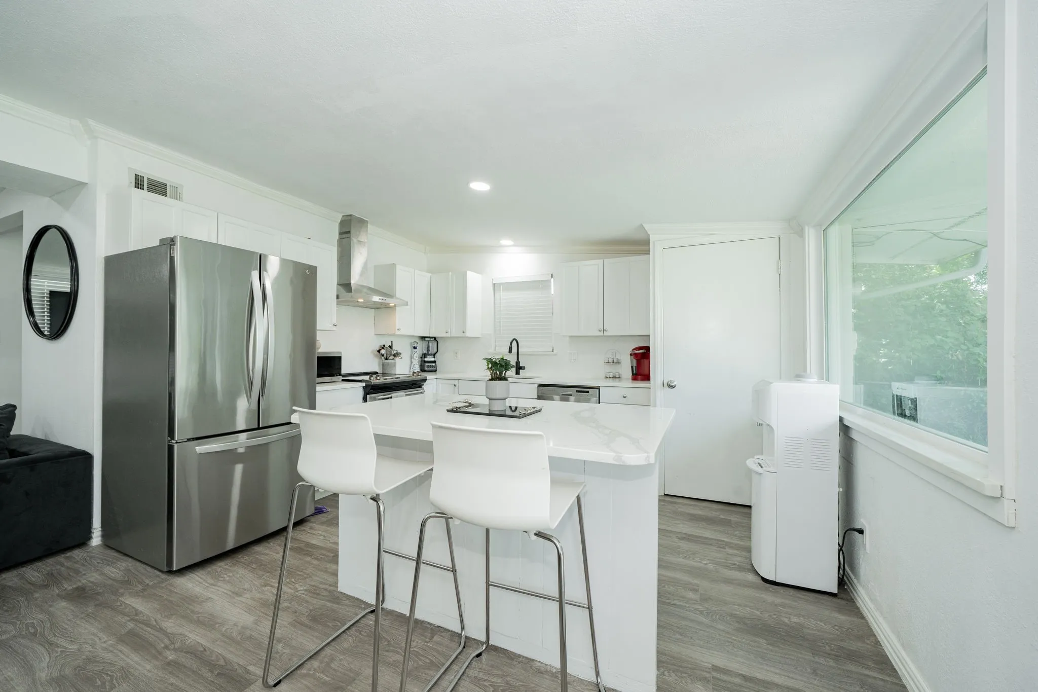 Kitchen featuring stainless steel appliances, white cabinets, a kitchen breakfast bar, wood finished floors, and wall chimney exhaust hood