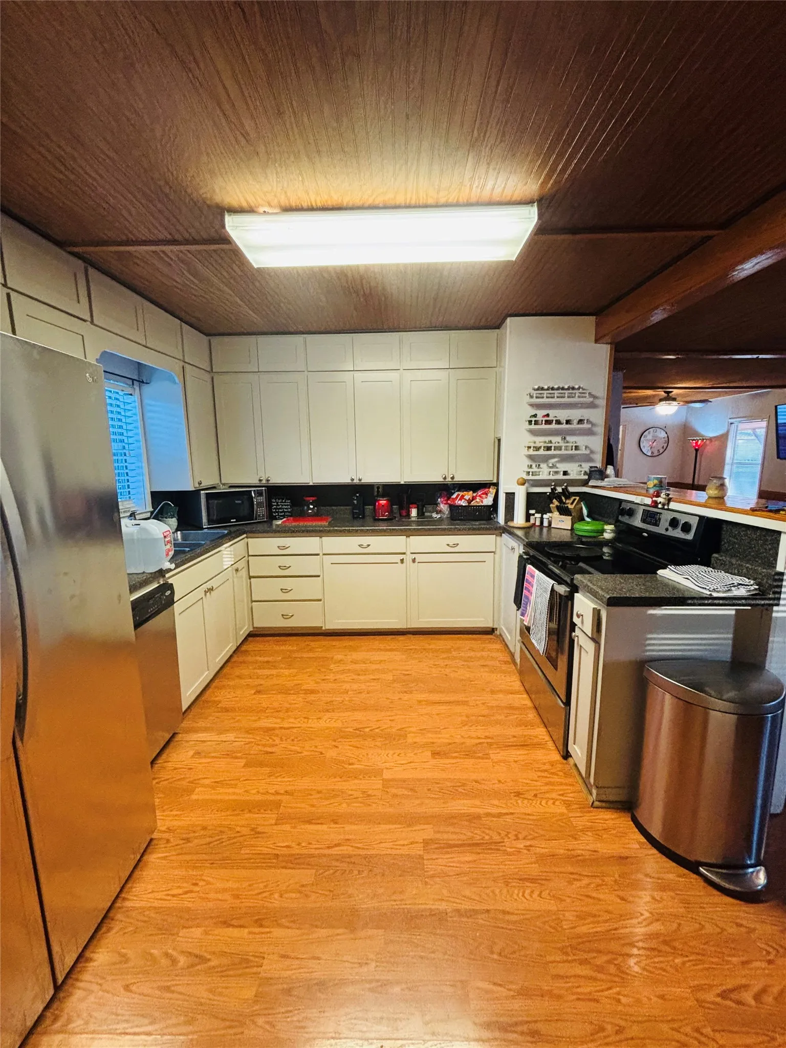 Wood-finish flooring, white cabinetry, dark countertops, stainless steel appliances, and a wood-paneled ceiling