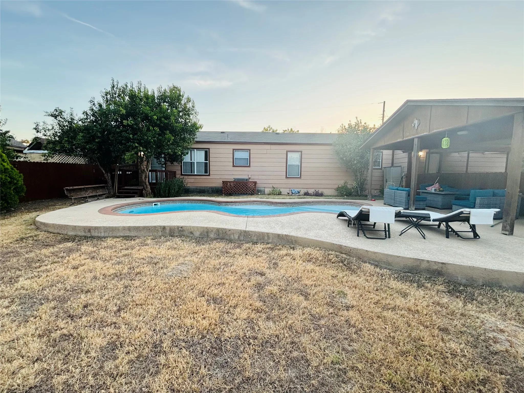 Freeform swimming pool with concrete decking, covered patio area, and mature trees