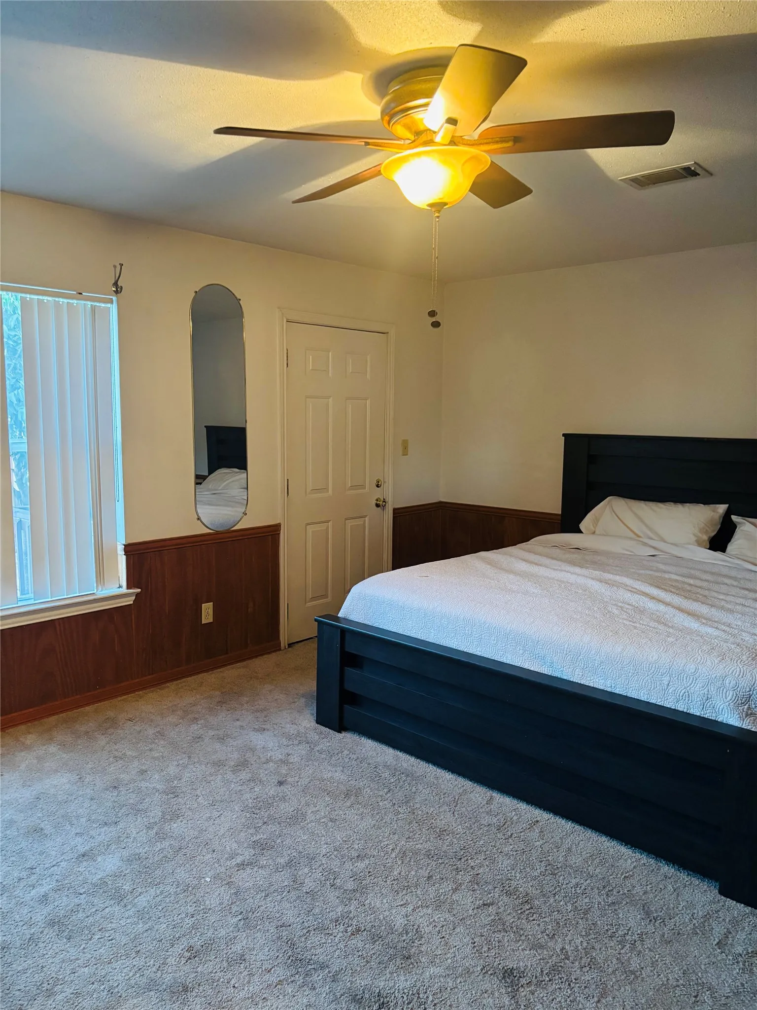 Carpeted flooring, wood-finish wainscoting, a ceiling fan with integrated lighting, and a window with blinds