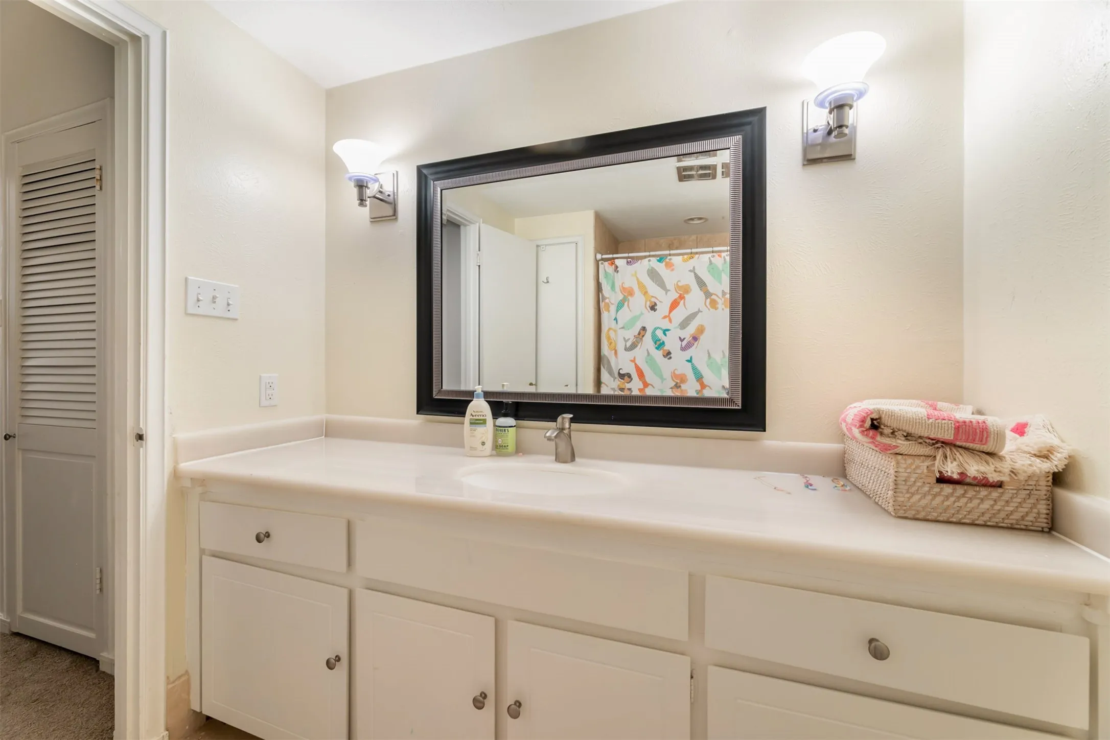 White vanity with integrated sink, framed mirror, and chrome wall sconces