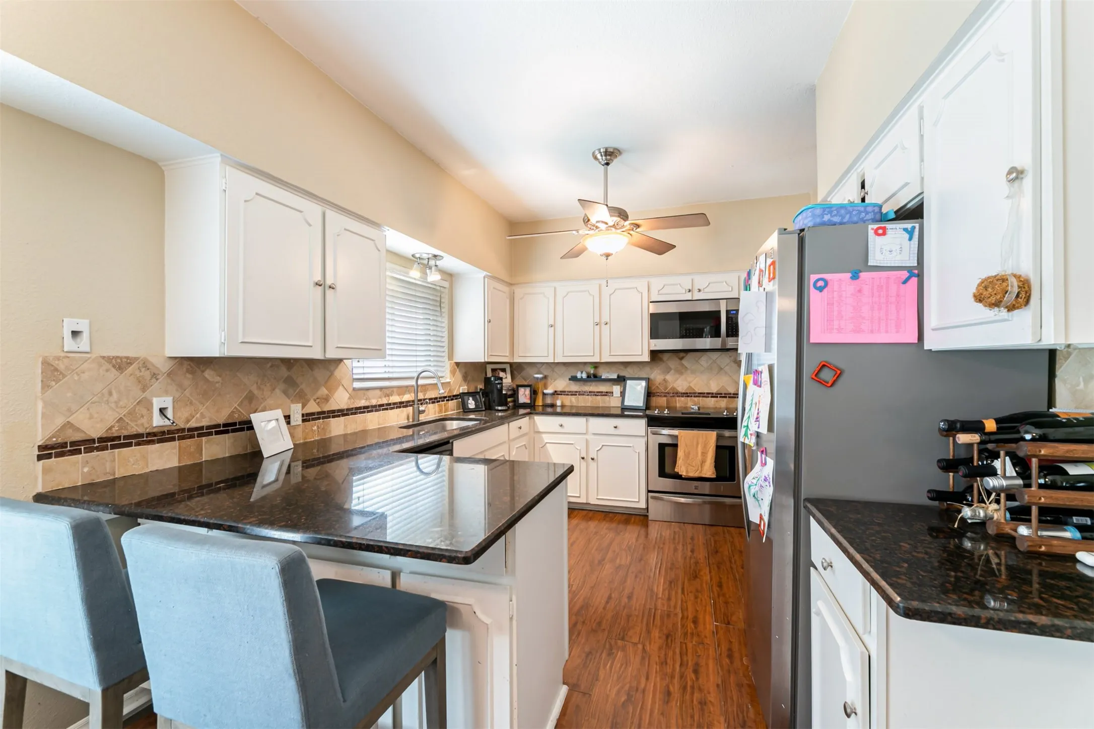 Kitchen featuring white cabinetry, dark stone countertops, stainless steel appliances, and wood-finish flooring