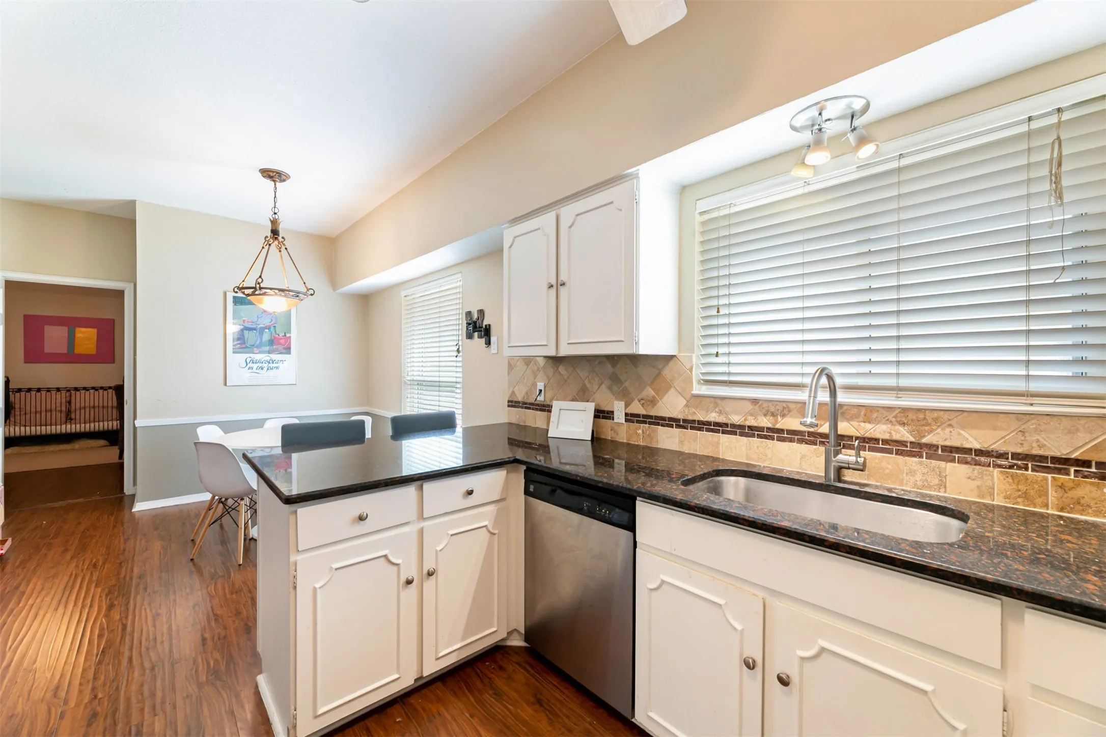 Kitchen featuring white cabinetry, dark countertops, a stainless steel sink, tile backsplash, and wood-finish flooring