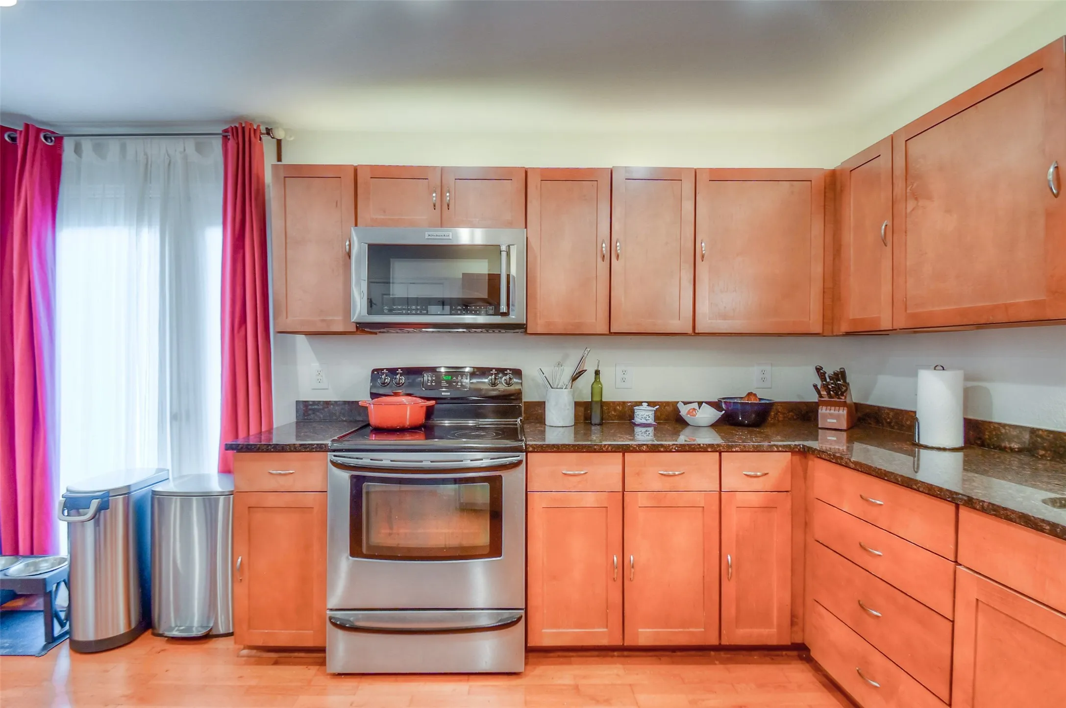 Kitchen featuring appliances with stainless steel finishes, brown cabinetry, light wood-style floors, and dark stone countertops