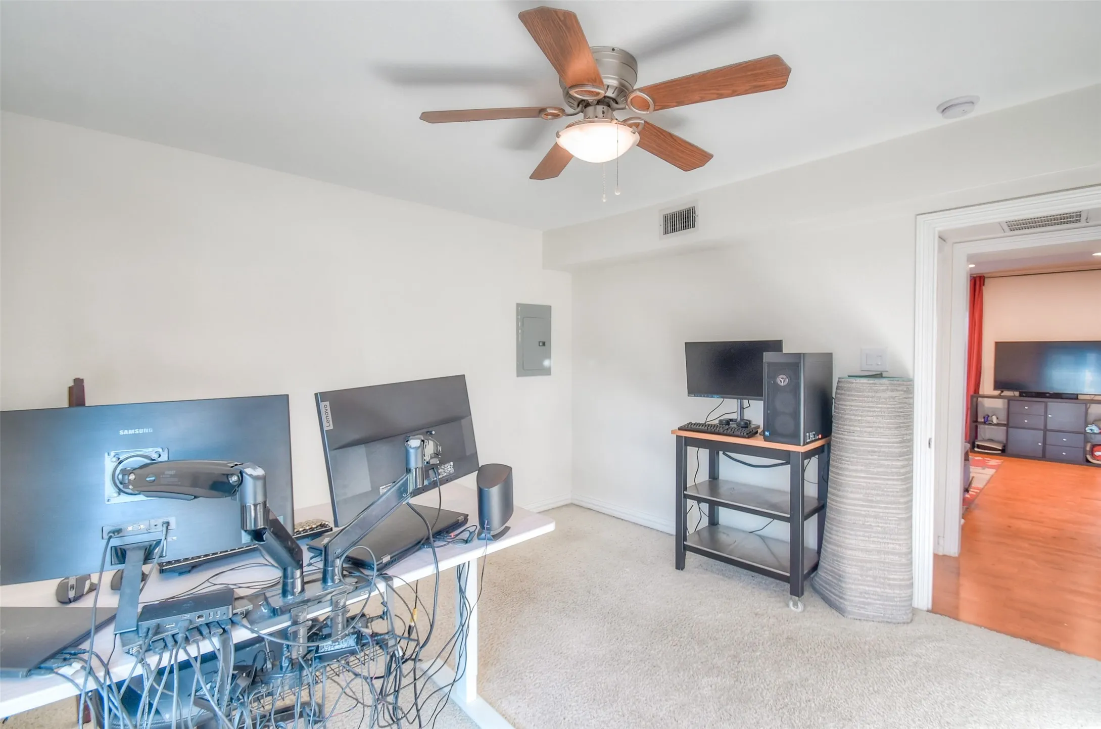 Office area with ceiling fan, electric panel, visible vents, and carpet flooring