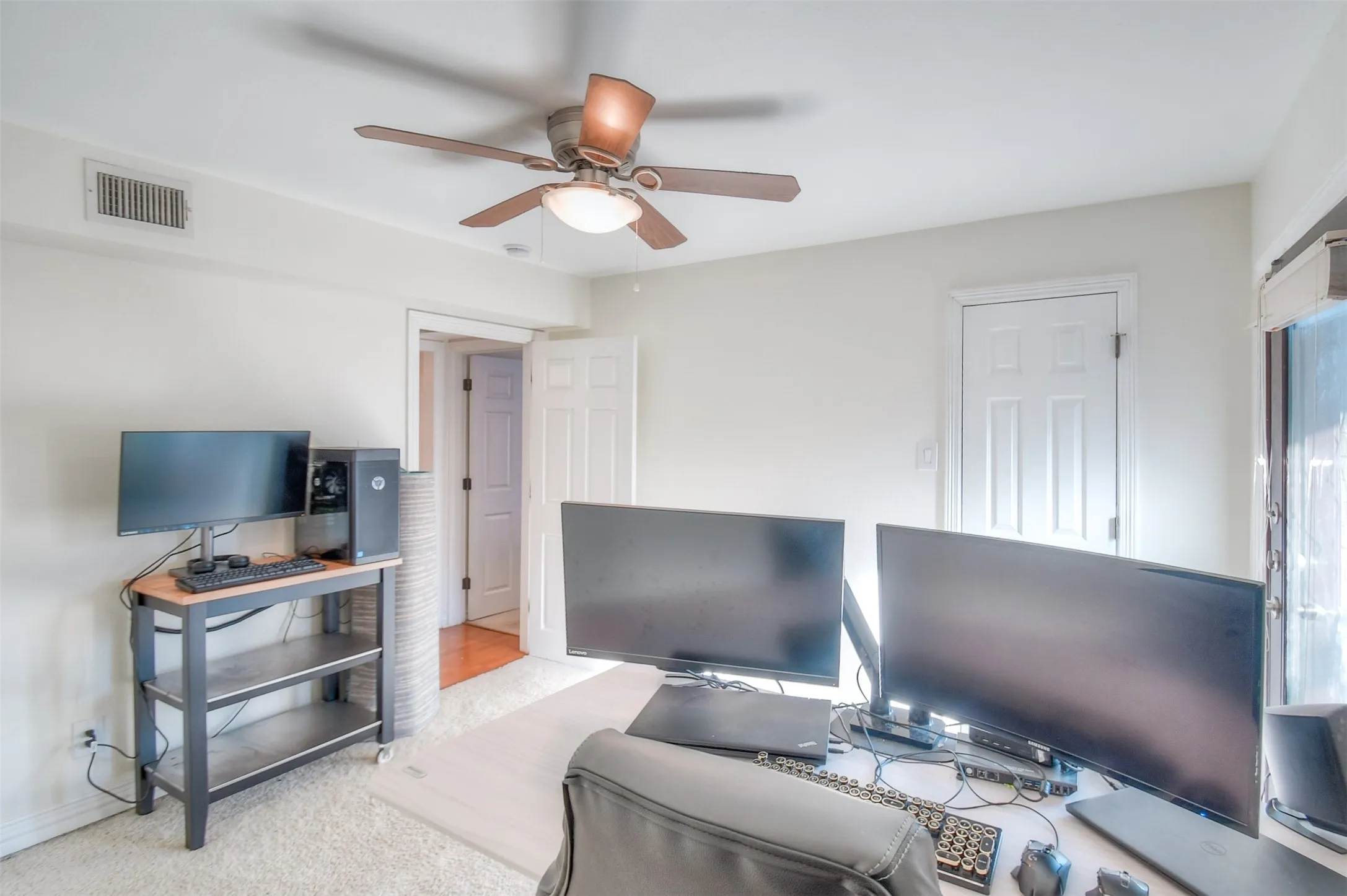 Carpeted home office with baseboards, visible vents, and a ceiling fan