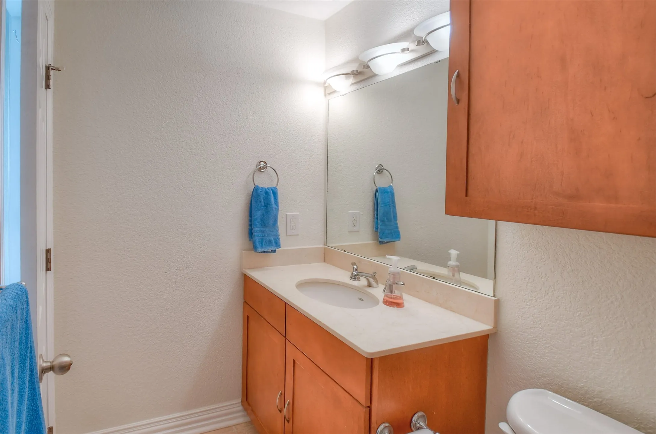 Bathroom with a textured wall, vanity, and toilet