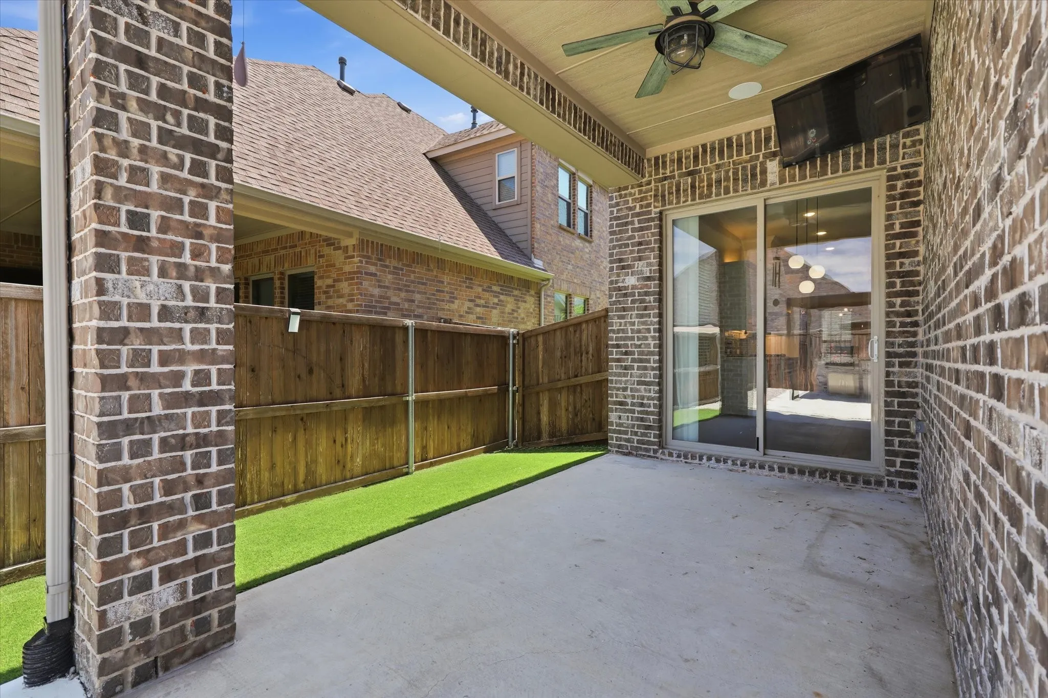 Covered patio featuring a concrete surface, brick columns, ceiling fan, and sliding glass doors.