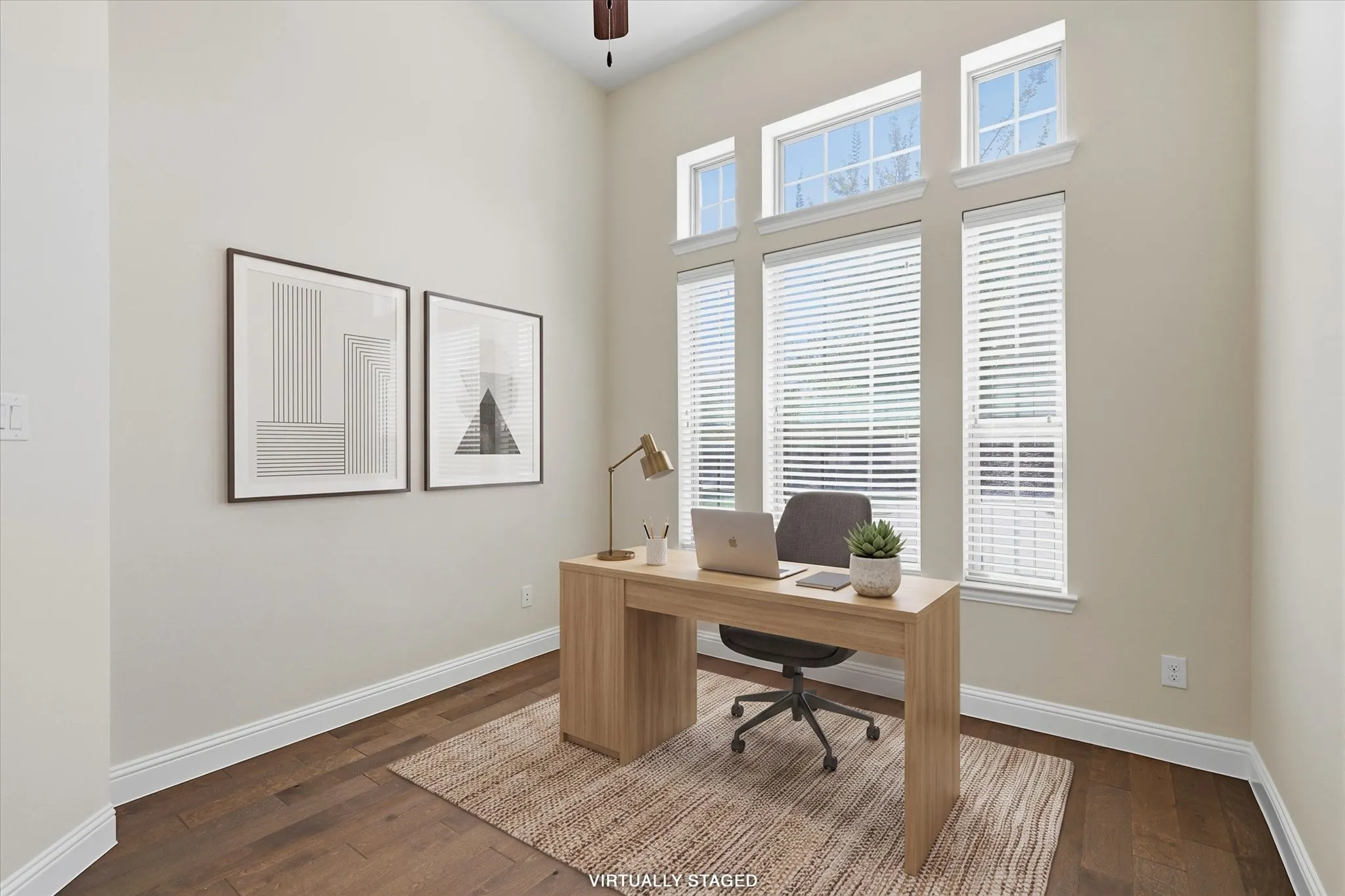 Separate home office features high ceilings, wood flooring, and multiple windows with white blinds. Virtually staged.