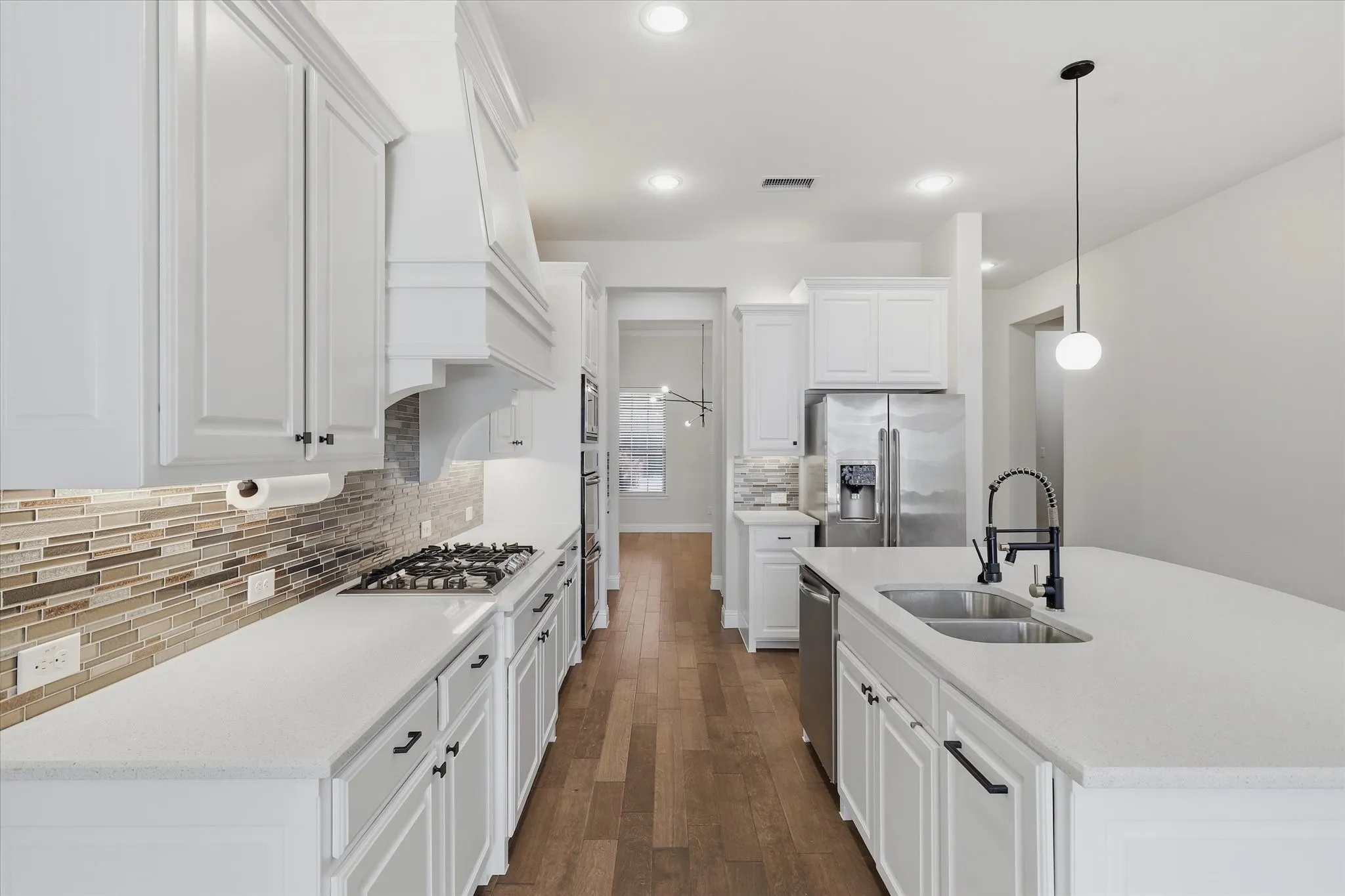 White cabinetry with dark hardware, gas range with custom vent hood, stainless steel appliances, white quartz countertops, wood flooring, and walk in pantry.