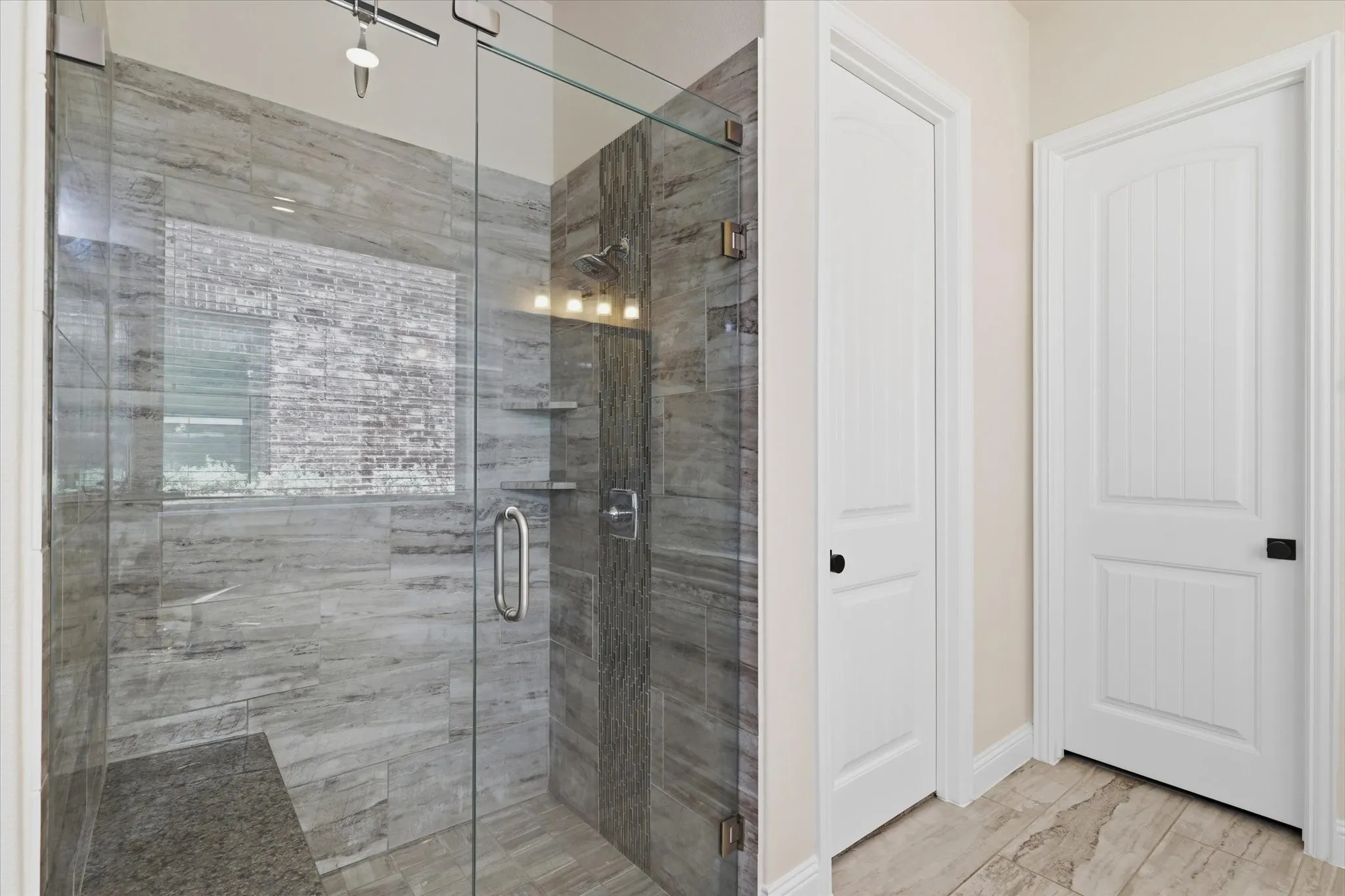 Glass-enclosed shower with tile surround, built-in shelving, and a tiled shower bench