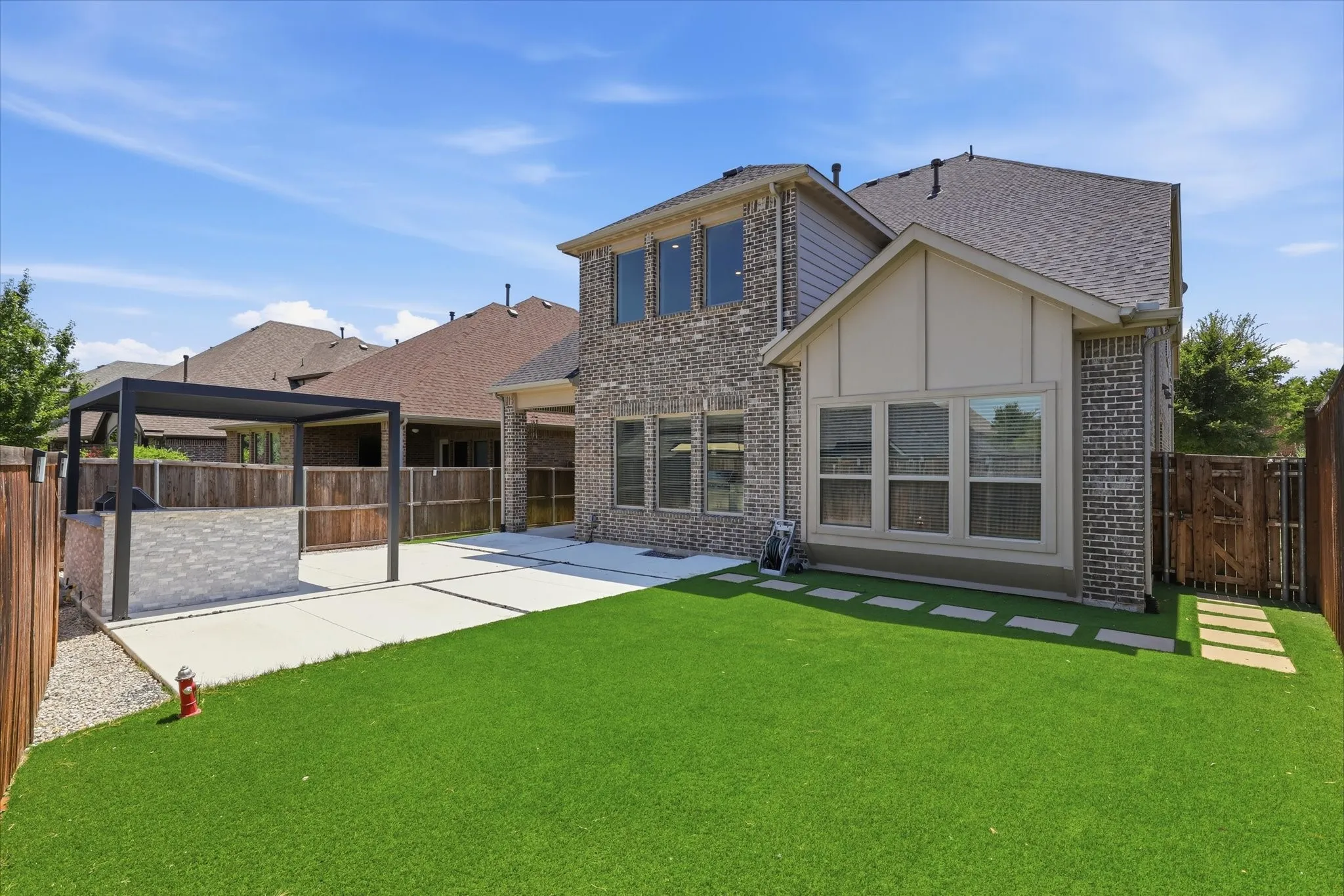 Spacious backyard featuring an outdoor kitchen with a pergola, concrete patio, artificial turf, and wood fencing