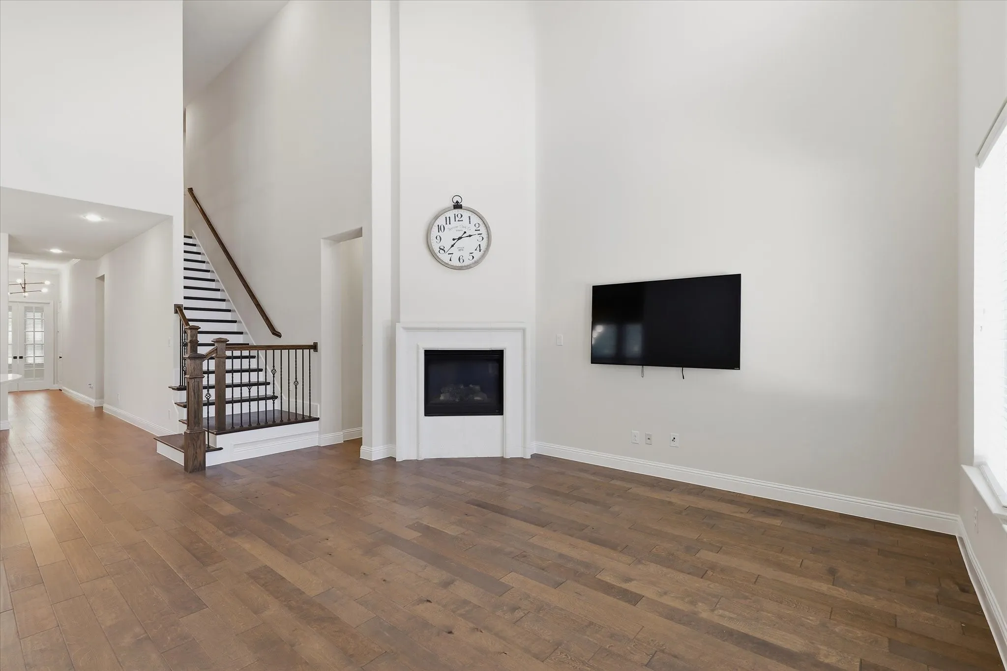 Expansive living area featuring high ceilings, wood flooring, a contemporary fireplace, and a staircase with dark wood and wrought iron balusters. TONS of natural light from the windows.