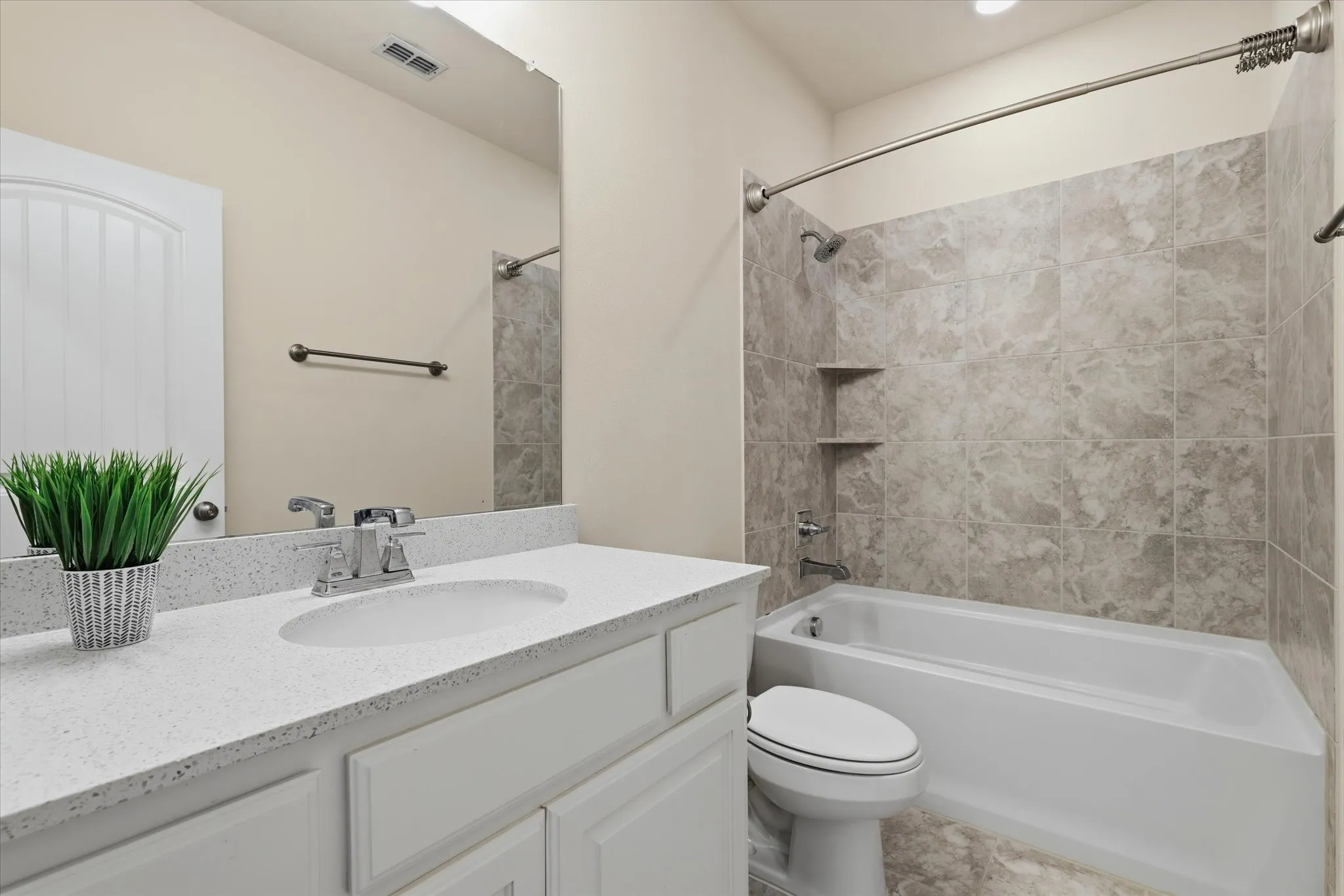 White vanity with a light speckled countertop, undermount sink, chrome faucet, and tub/shower combo.