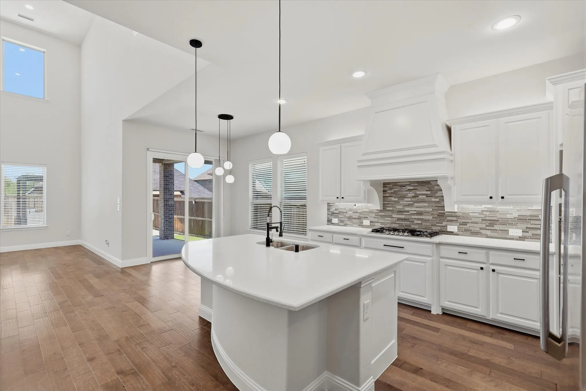 Kitchen and breakfast area with wood flooring, white cabinetry with dark hardware, kitchen island with integrated sink, quartz countertops and sliding glass patio door