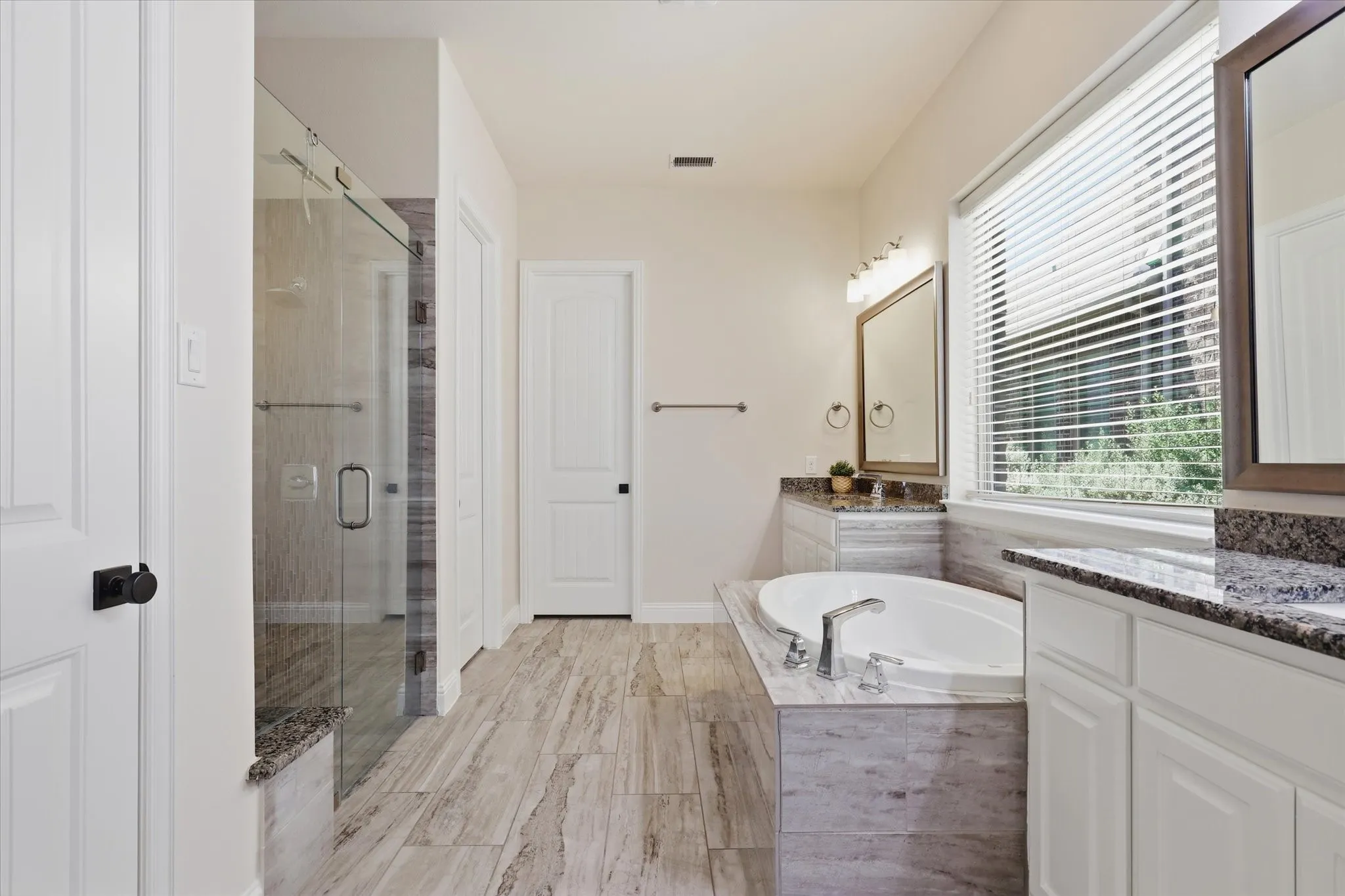 Walk-in shower with glass enclosure, soaking tub, dual vanities with stone countertops, and wood-finish flooring.  Large Walk In Closet.