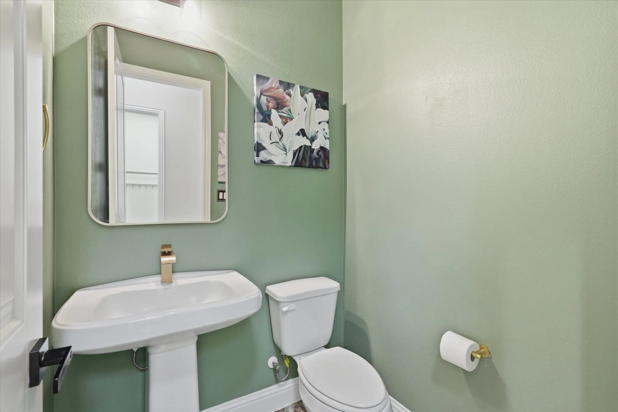 Pedestal sink with gold-tone faucet, wall-mounted mirror.