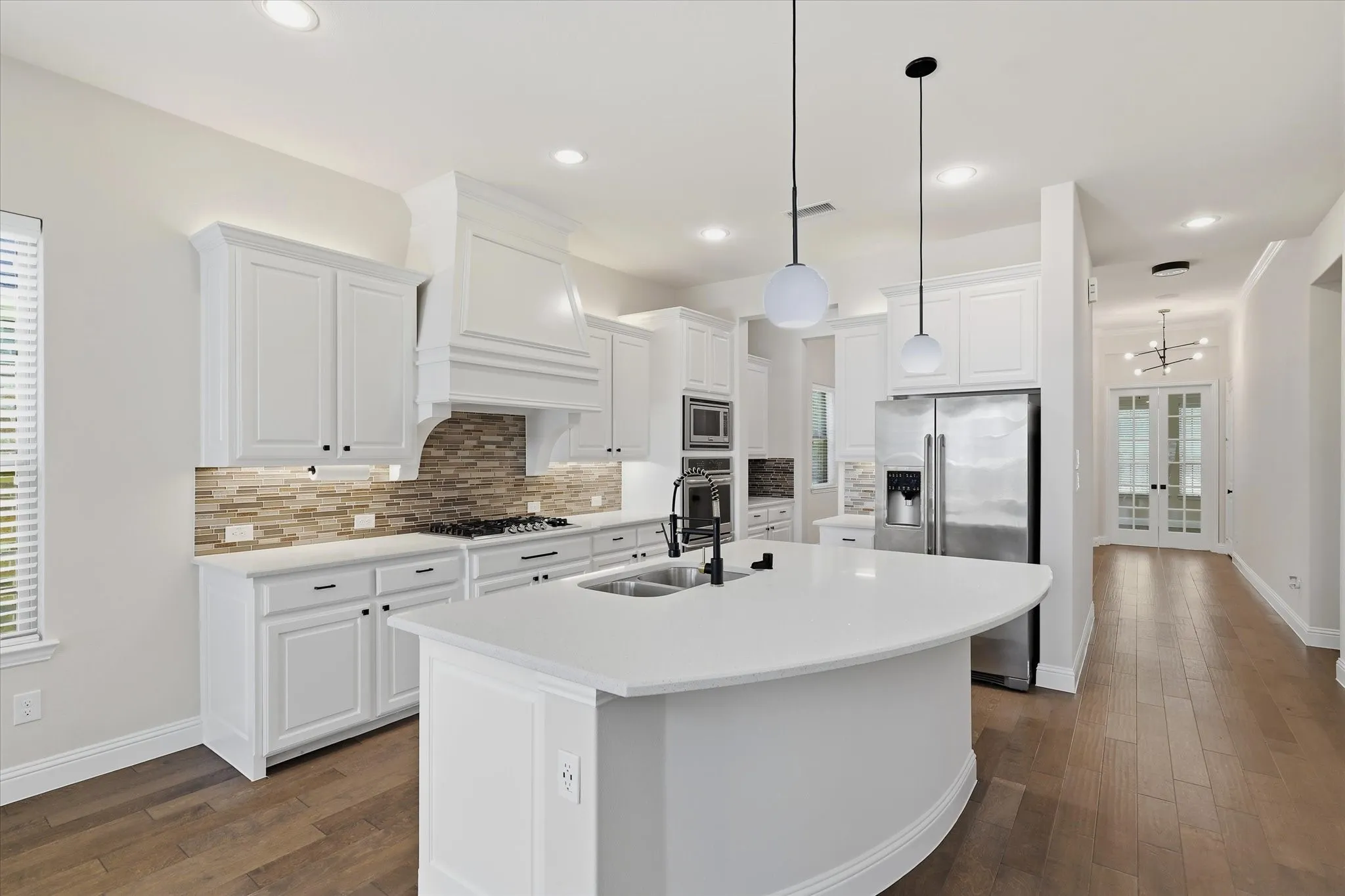 This open concept kitchen features White shaker cabinetry, built-in stainless steel appliances, recessed lighting, wood flooring, and quartz countertops.